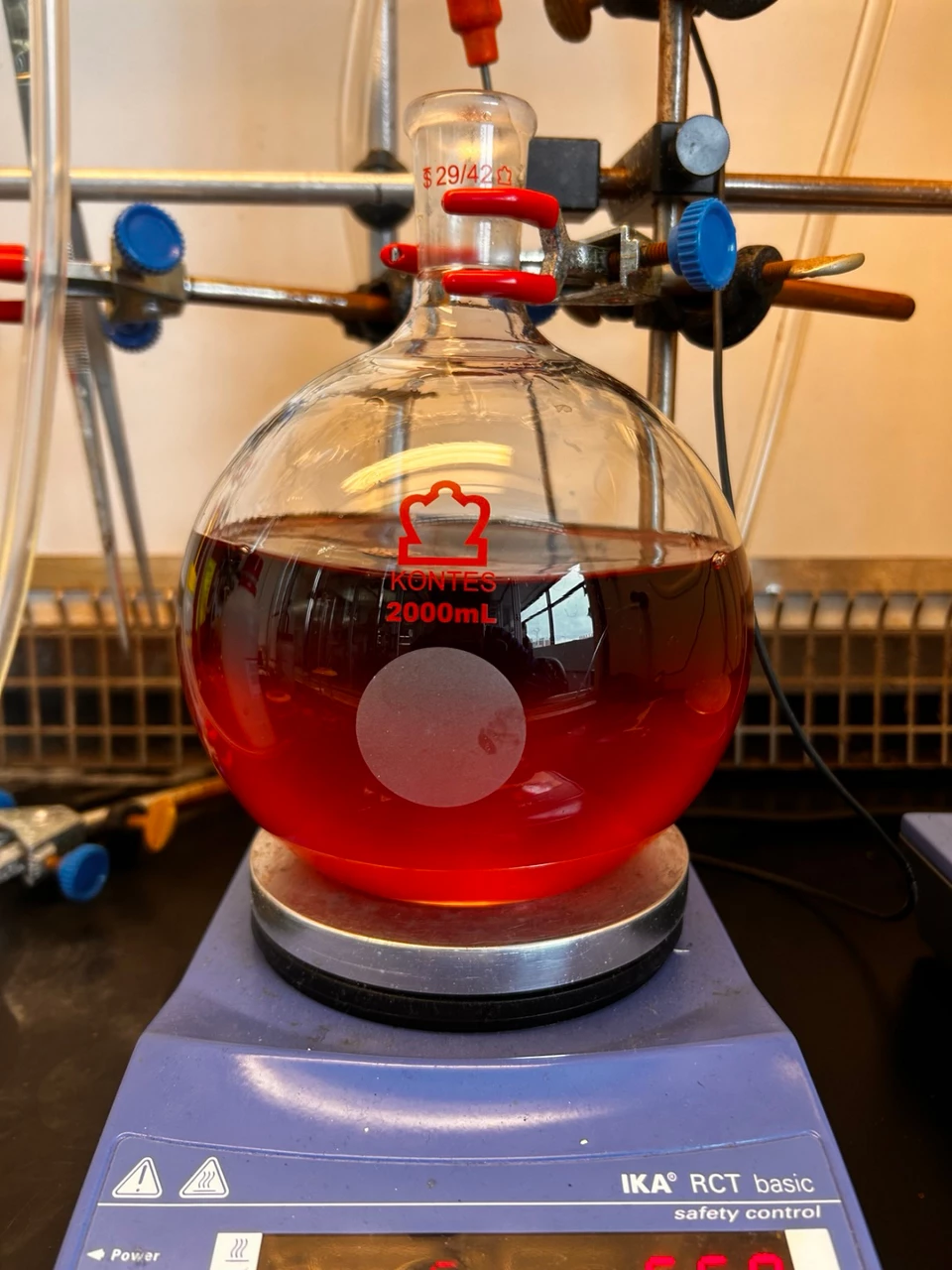 A round-bottom flask, more than half full with red liquid, sits atop a lab scale.