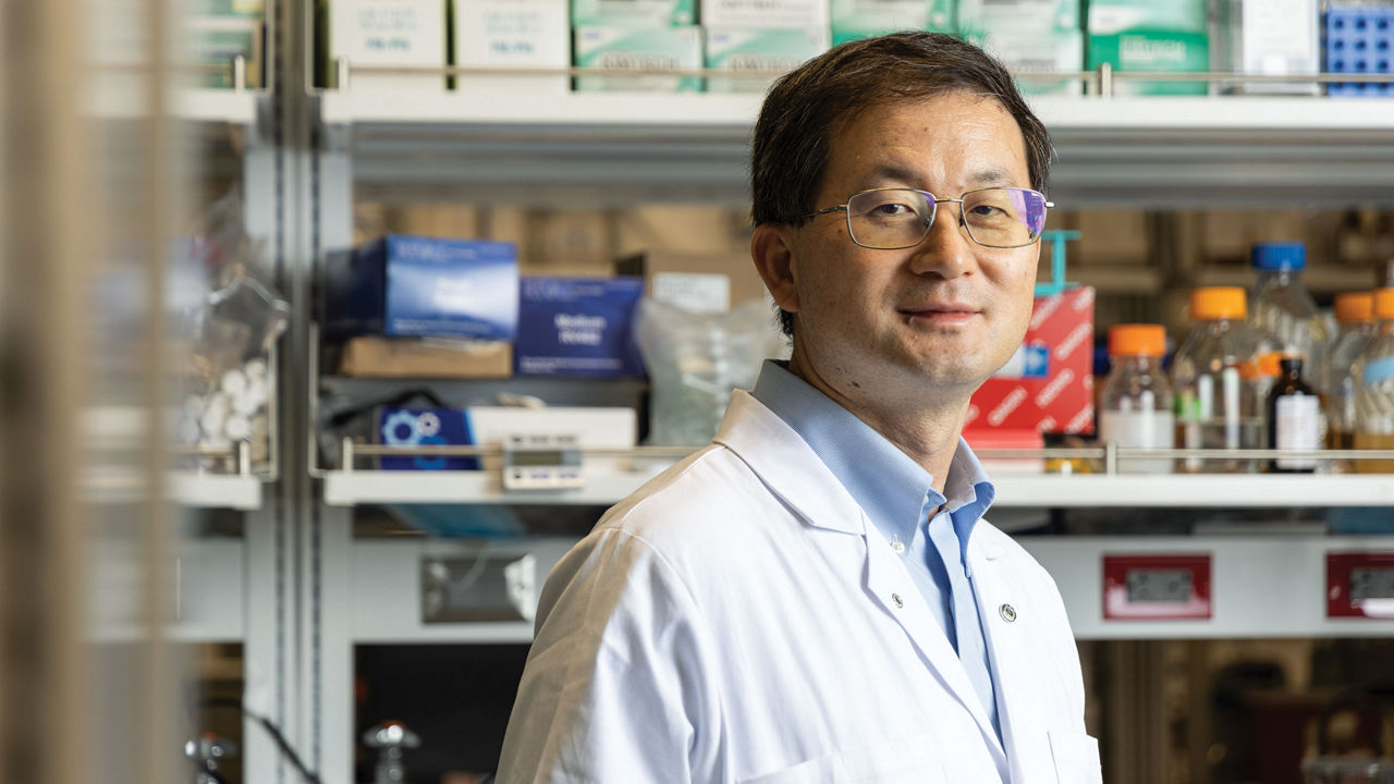 Liangfang Zhang, in a white lab coat and glasses, stands in a laboratory.