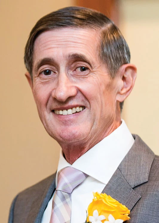 Thomas L. Penner wears a gray suit, white shirt, and pink tie, and smiles at the camera.