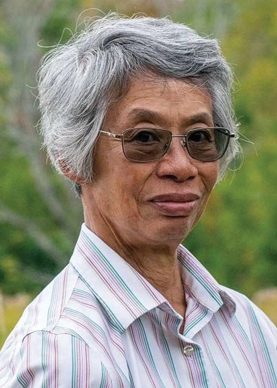 Jeanne B. Li wears a striped shirt and glasses, and smiles at the camera.