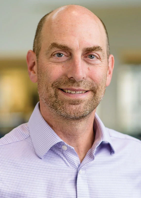 Joel Tickner, wearing a checkered dress shirt, poses for a portrait.