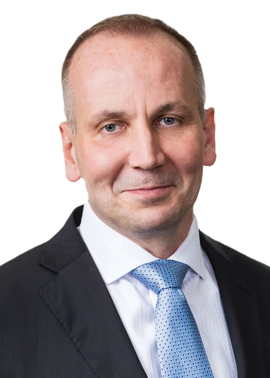 Slawomir Platta, wearing a white dress shirt, a blue tie, and a dark suit jacket, poses for a portrait.