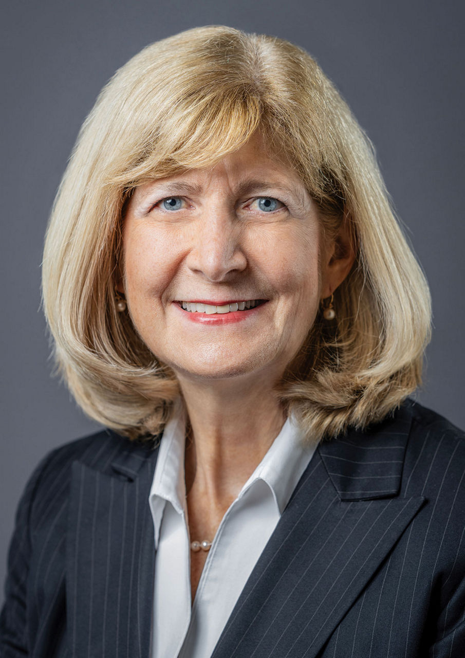 A woman wearing a black blazer smiles at the camera for a formal portrait shot.