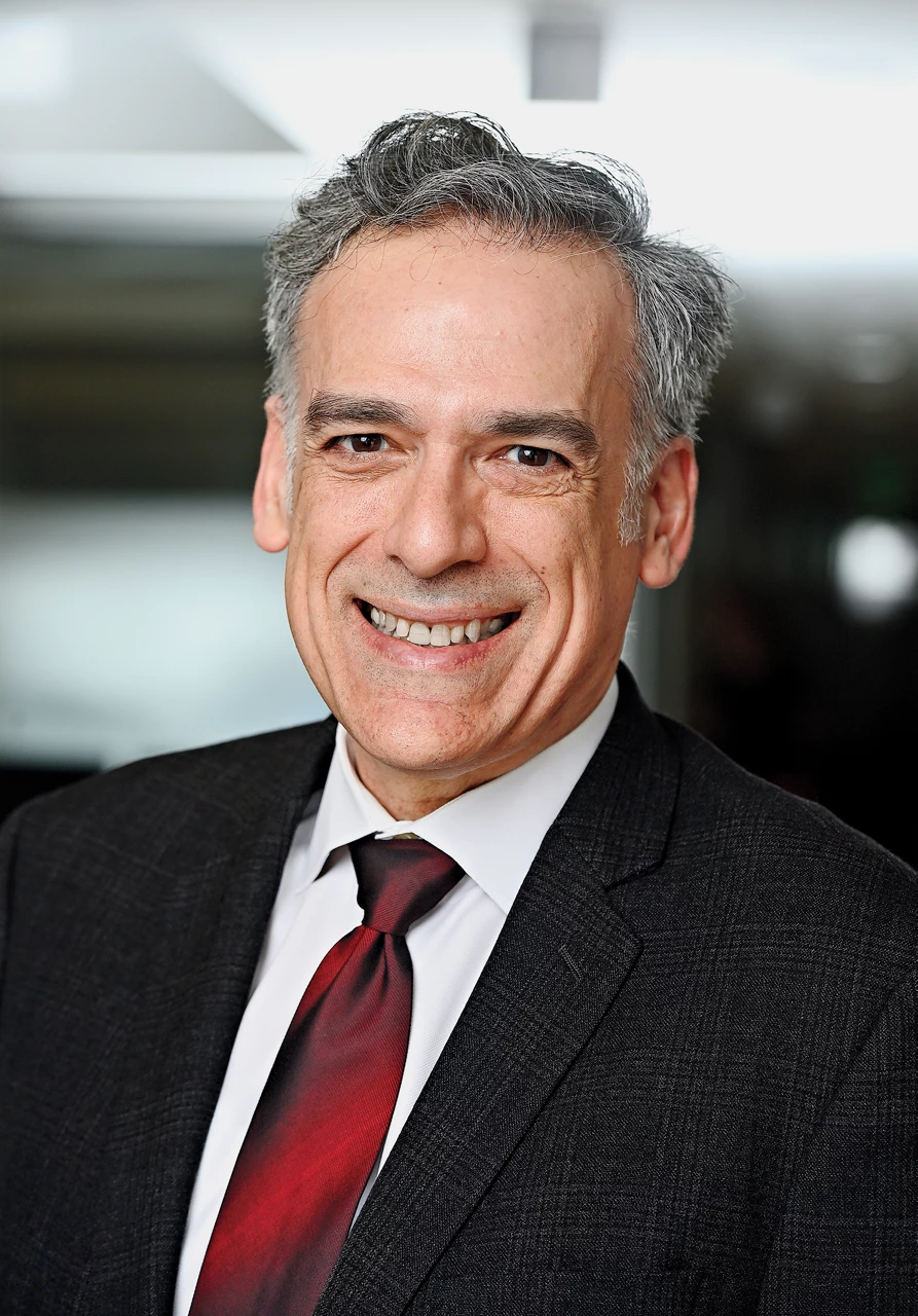 Rigoberto wears a dark suit and a tie and smiles at the camera.