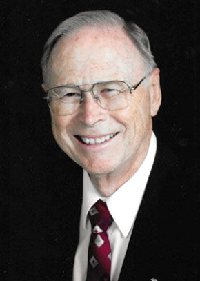Alan F. Rogers wears a white tie, red tie, and dark jacket and smiles at the camera. 