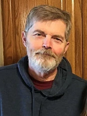 Kenneth W. Raymond wears a black hoodie and red t-shirt and looks at the camera. 