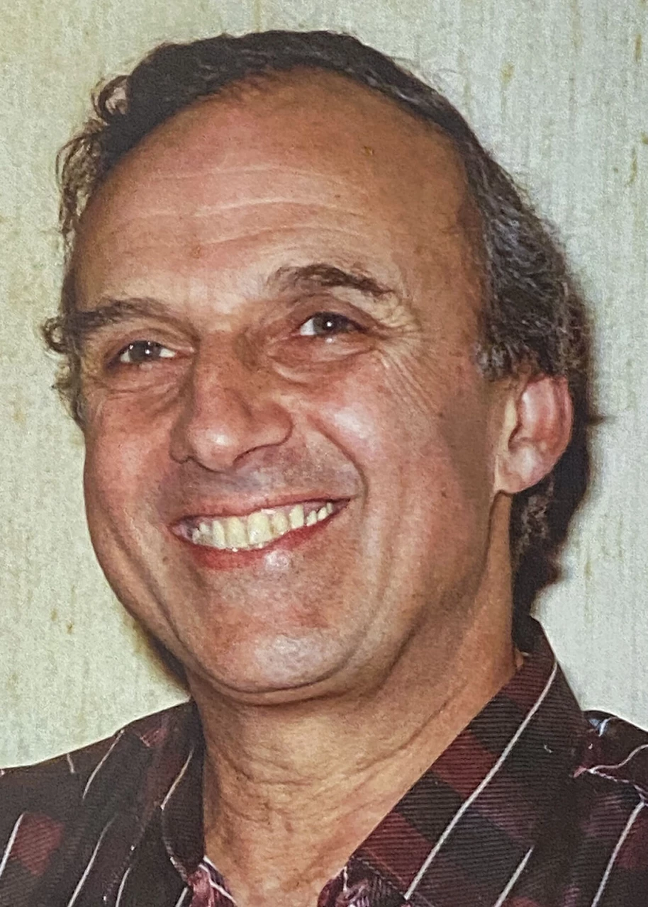 <i>Michael Besso wears a check red, black, and white shirt, and gazes to the side of the camera.</i>
