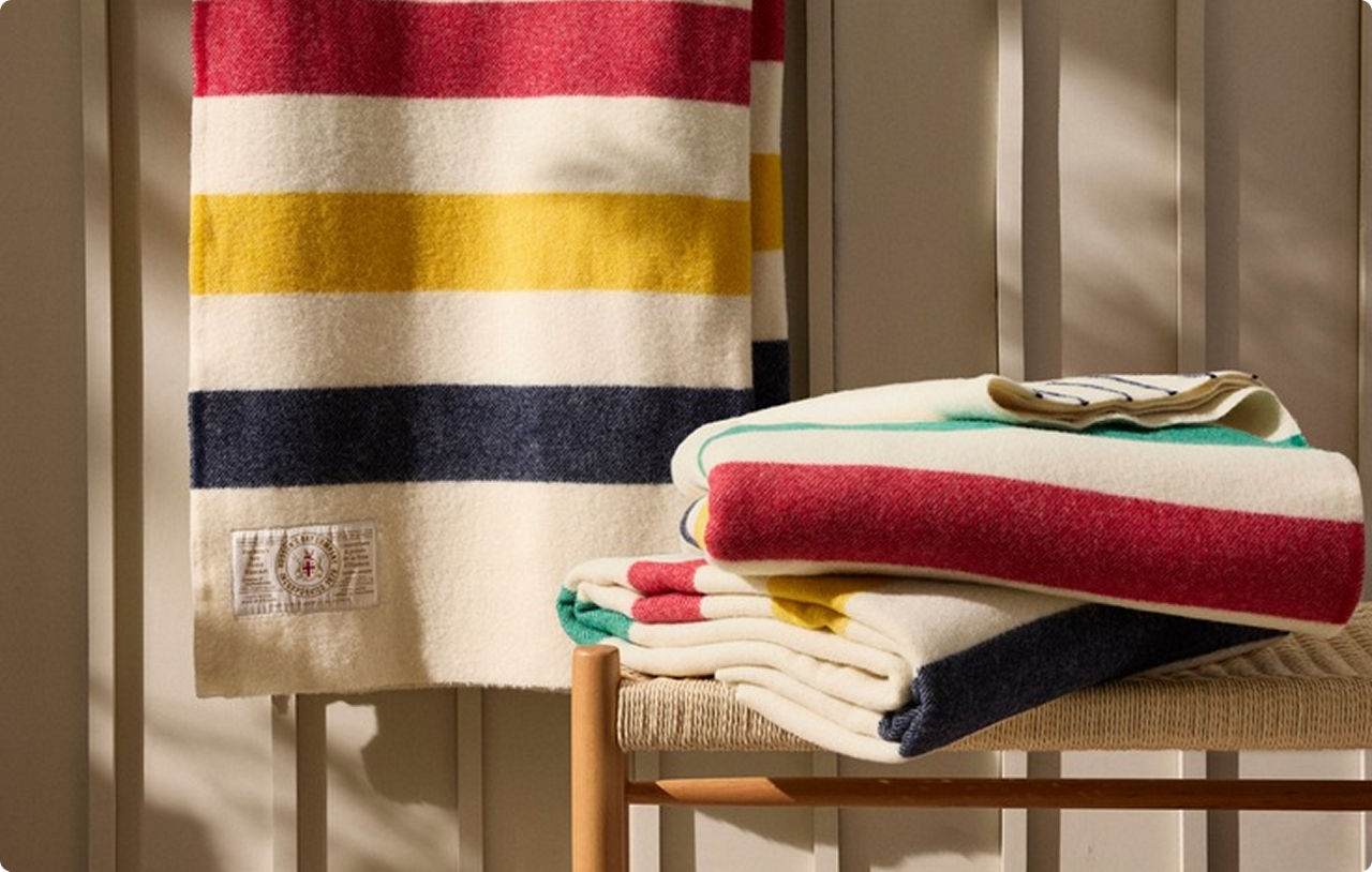 Two Hudson's Bay Stripes blankets stacked on a chair beside a blanket hanging on a rack.