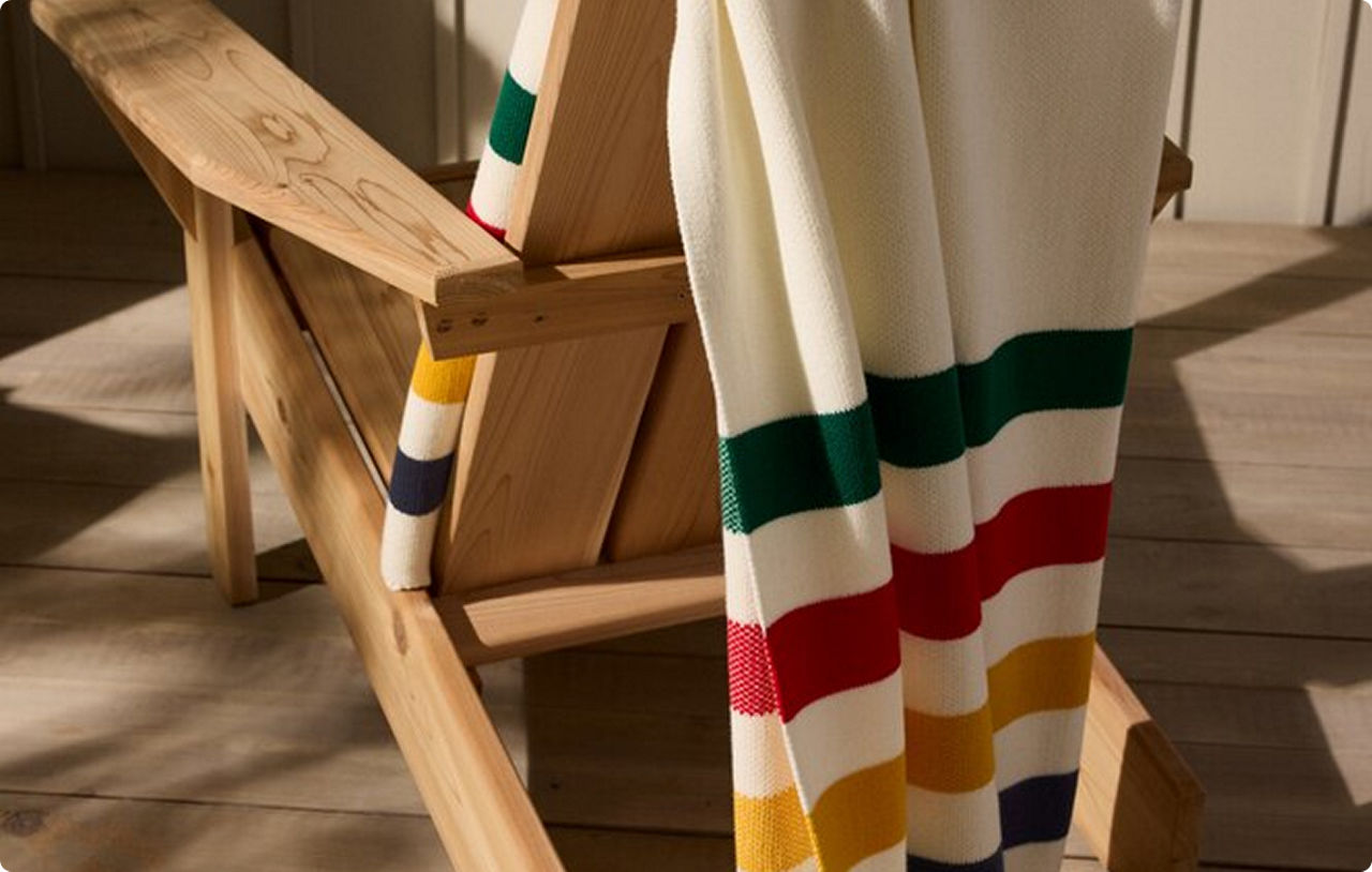 A Hudson's Bay Stripes blanket hanging over the back of a wooden Muskoka chair.