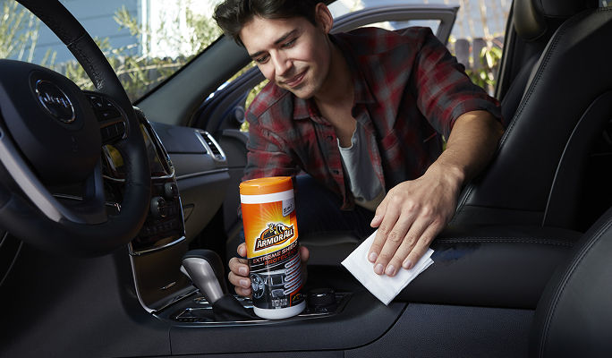 Une personne tenant une bouteille de nettoyant pour l'intérieur d'une voiture tout en essuyant le tableau de bord d'un véhicule à l'aide d'un chiffon.