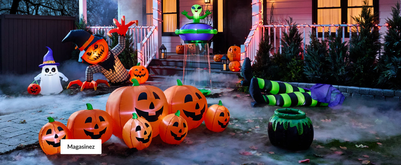 Un décor d’Halloween devant une maison décorée de guirlandes de lumières orange qui comprend des citrouilles d’Halloween gonflables illuminées, un personnage géant à tête de citrouille, un fantôme portant un chapeau de sorcière et tenant un panier pour passer l’Halloween, une décoration d’un extra-terrestre, les jambes d’une sorcière portant des bas rayés à côté d’un chaudron.