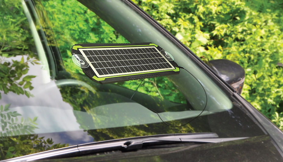 A Noma 5W solar battery trickle charger on the windshield of a black car.