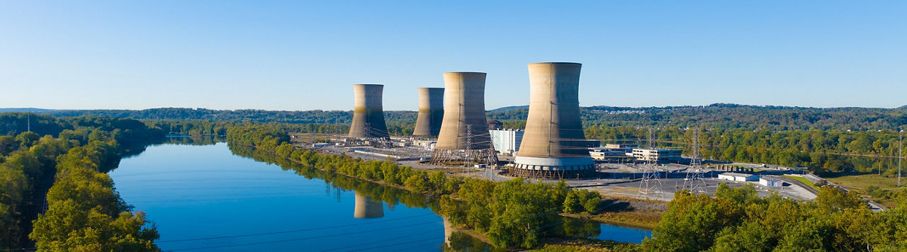 wide shot of 4 cooling towers along river during the day