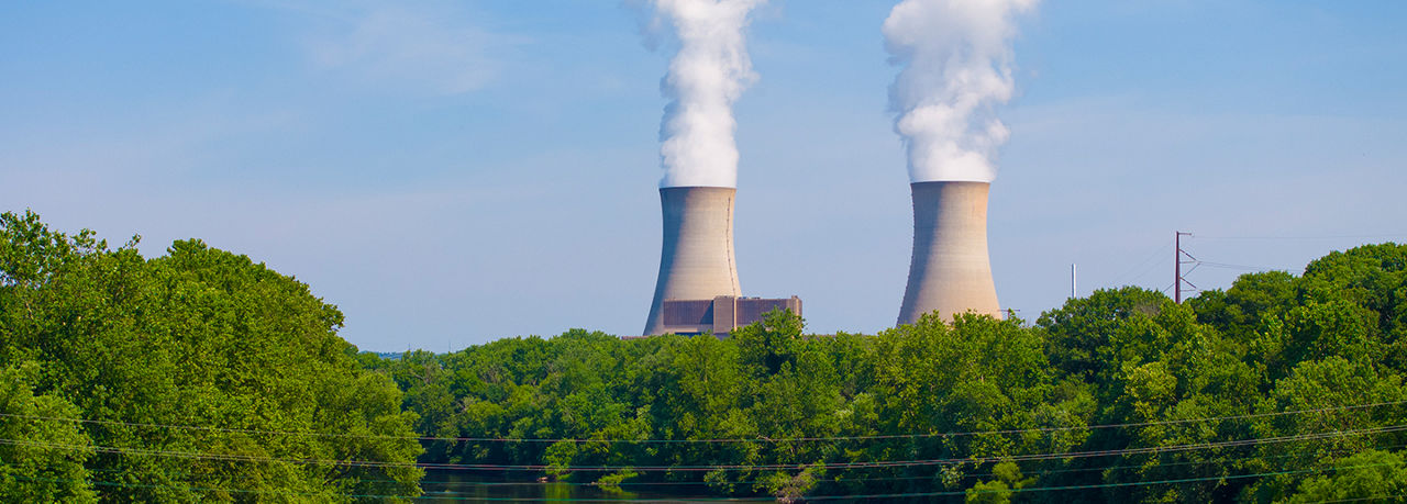 Two cooling towers with water vapor behind a bridge and trees