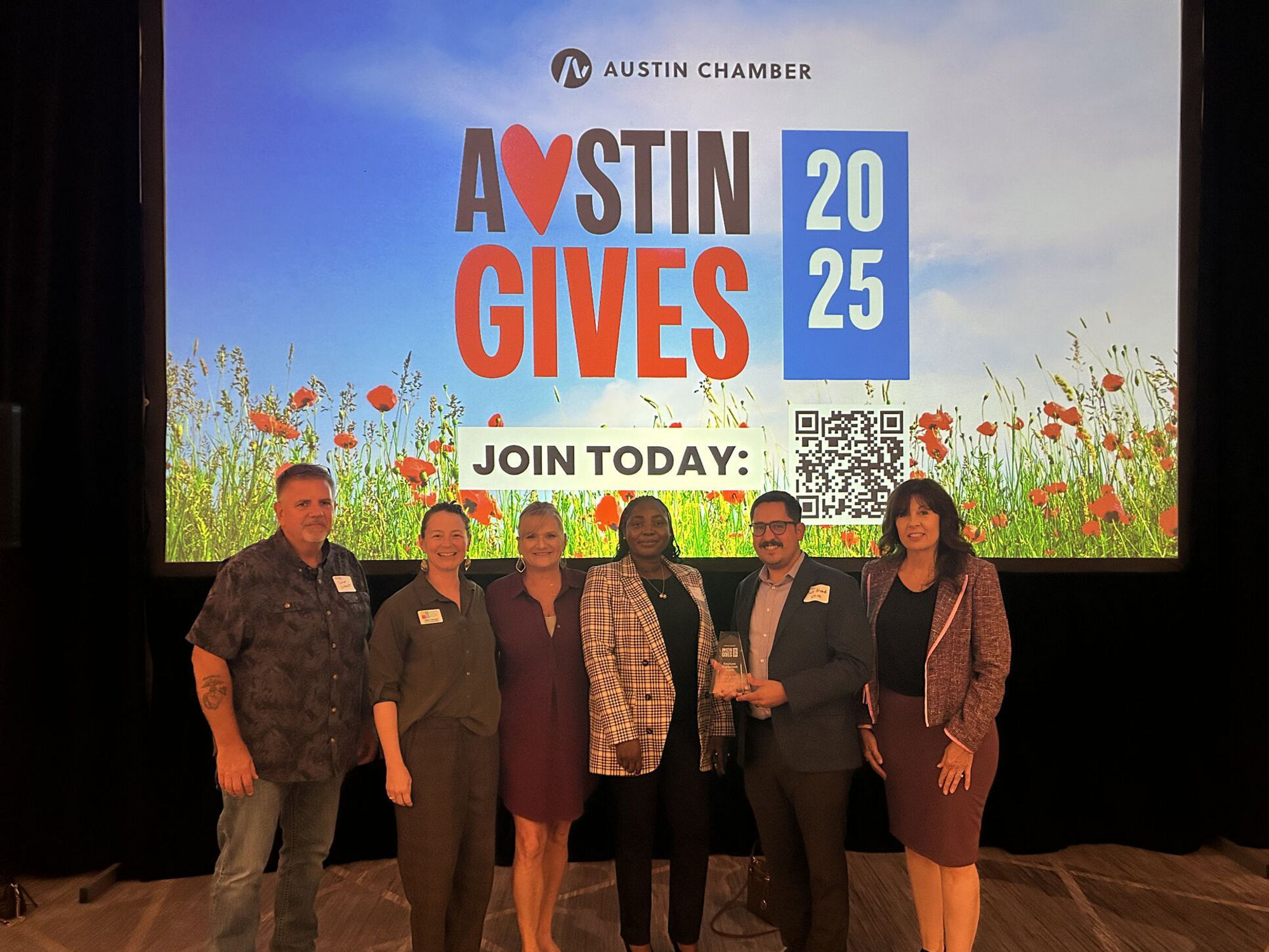 Six individuals standing in front of a large screen displaying 'Austin Gives 2025', as EPCOR accepts award for promoting community engagement at the Austin Chamber event.