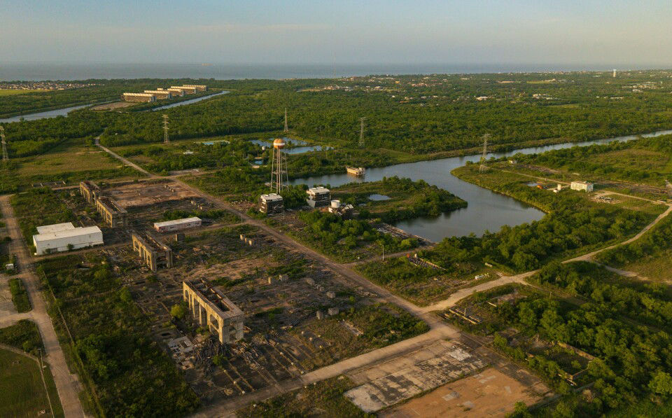 Aerial photo of a proposed desalination facility site featuring abandoned industrial buildings, dense vegetation, and surrounding waterways.