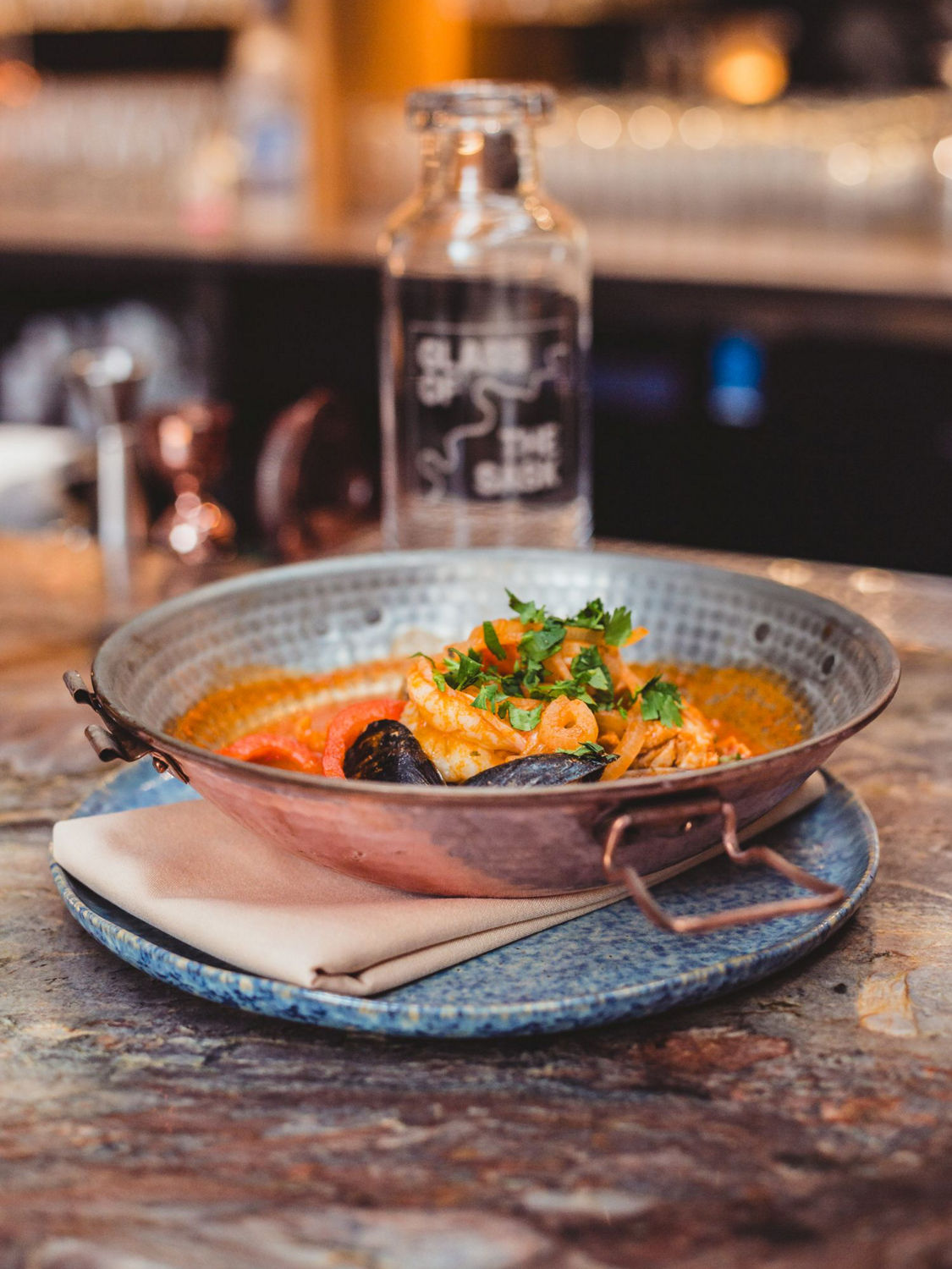  Seafood dish served in a metal pan, garnished with fresh herbs and mussels, created for Glass of the Sask.