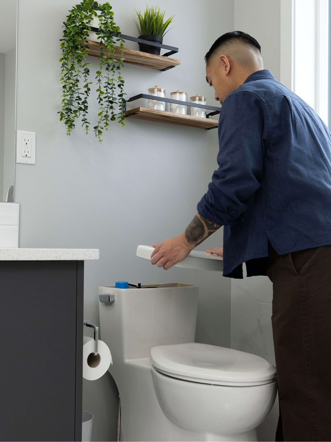 Someone in a bathroom lifting up the lid of toilet tank 