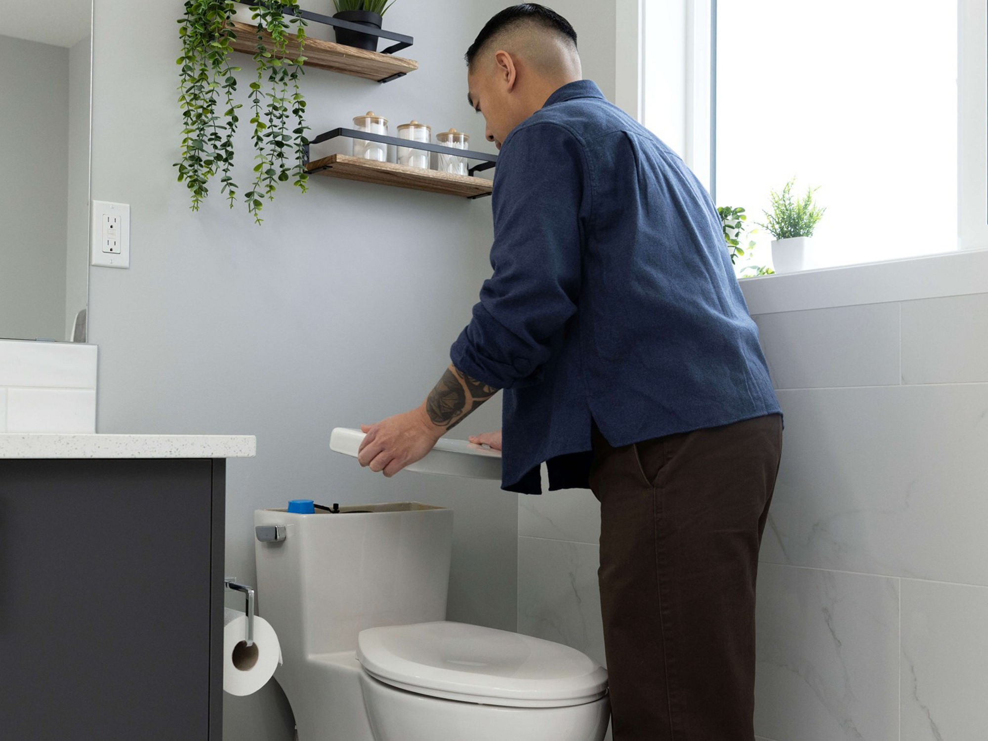 Someone in a bathroom lifting up the lid of toilet tank 