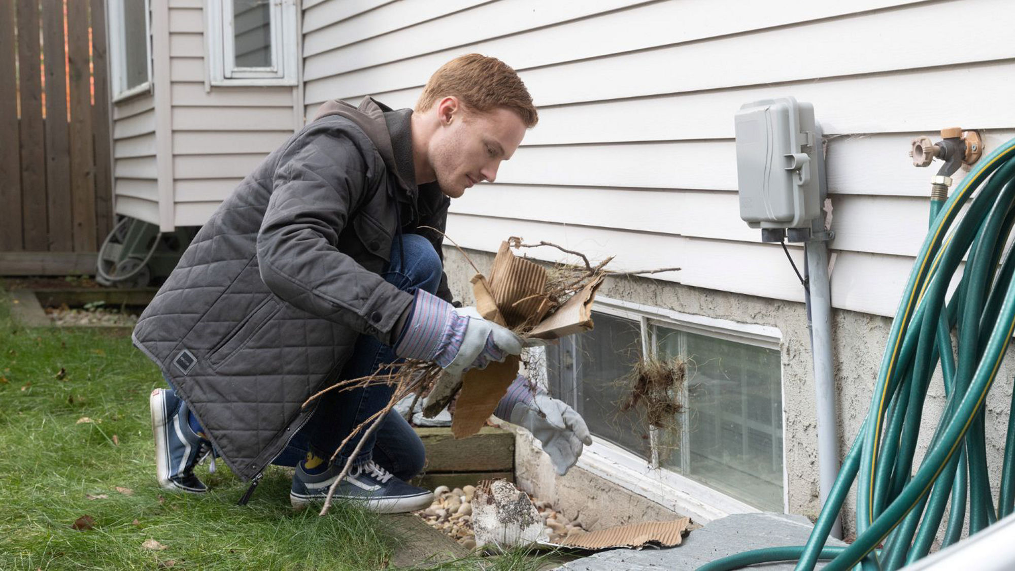 A homeowner clears debris from a window well to improve drainage and help prevent water buildup.