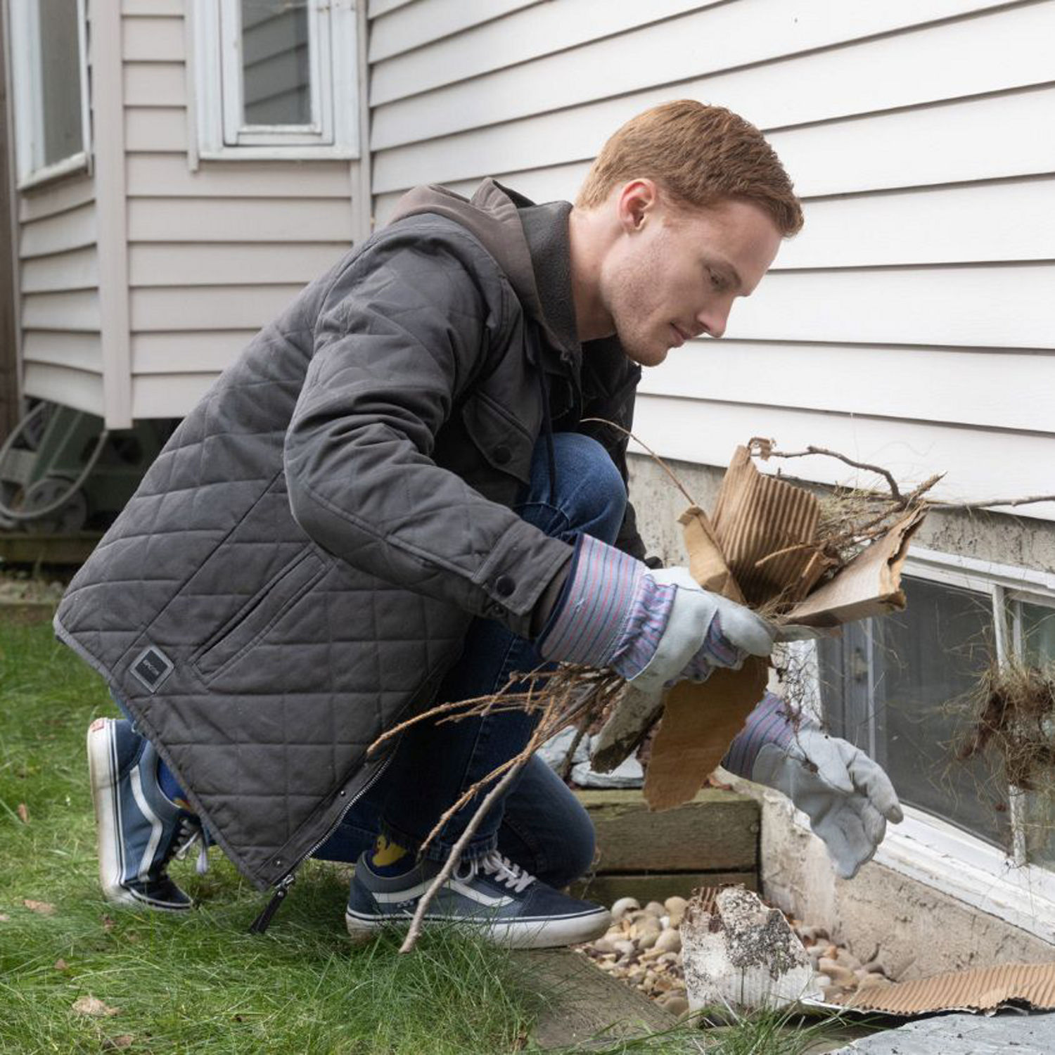 A homeowner clears debris from a window well to improve drainage and help prevent water buildup.