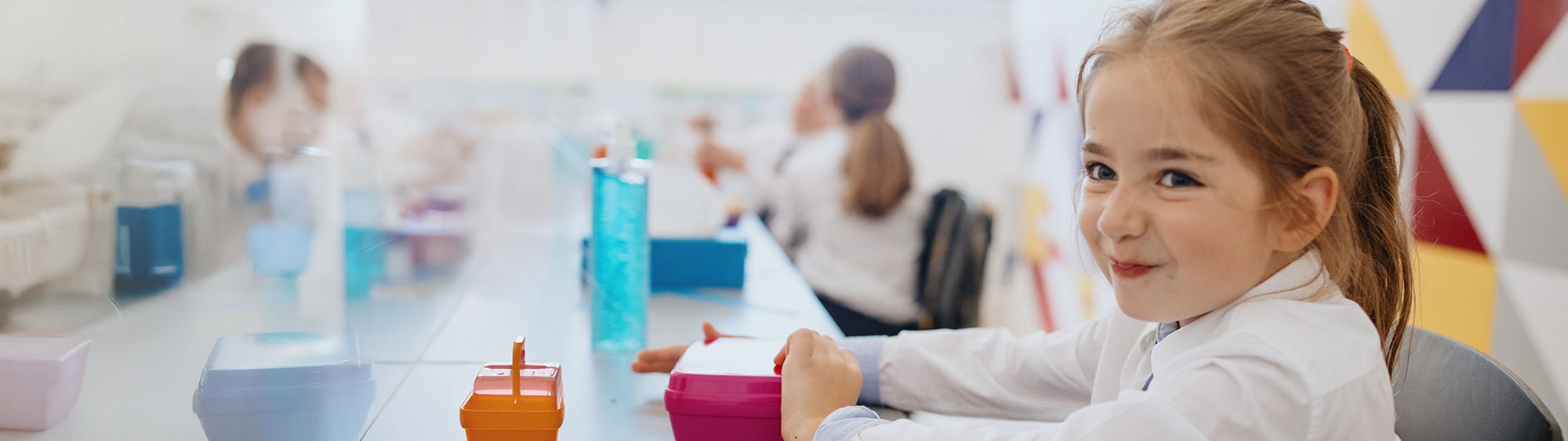 A young girl smiles during school lunch.