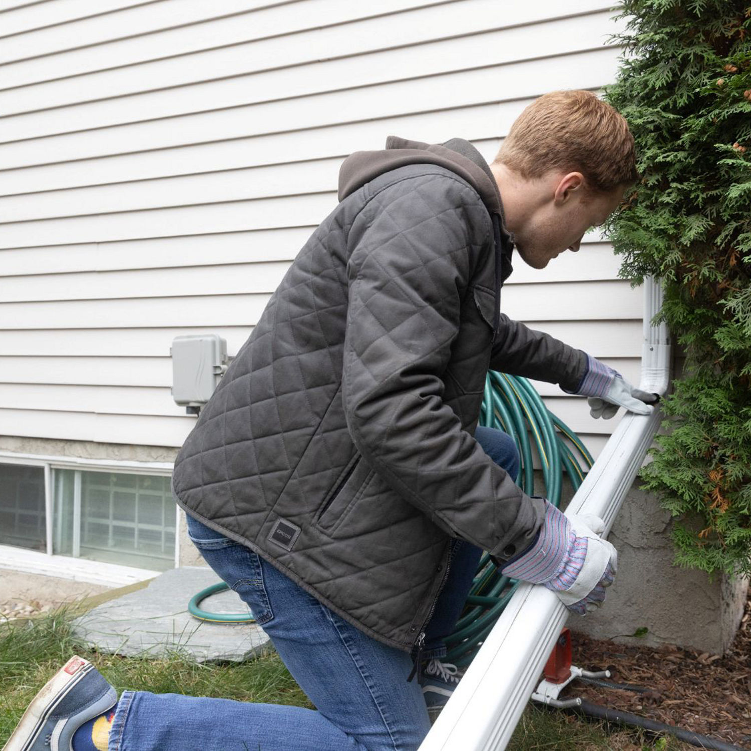 A person checking the downspout is connected correctly on their home before a storm.