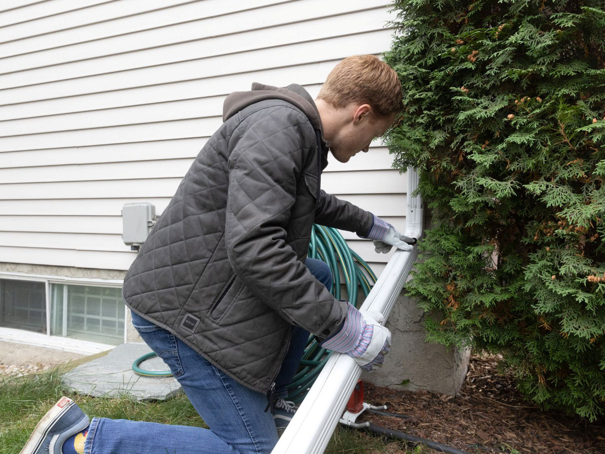 A person checking the downspout is connected correctly on their home before a storm.