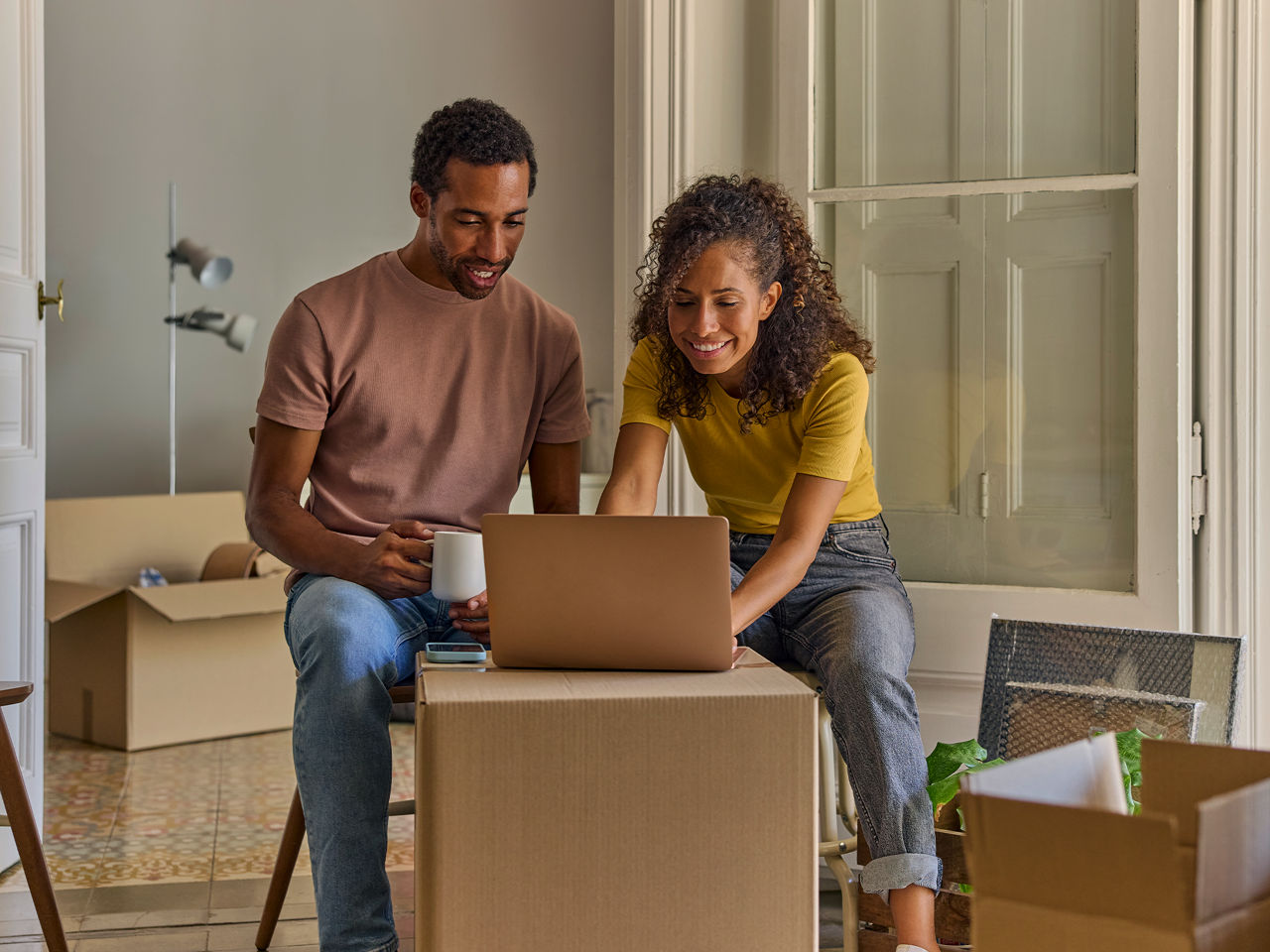 Couple surrounded by moving boxes working on laptop.