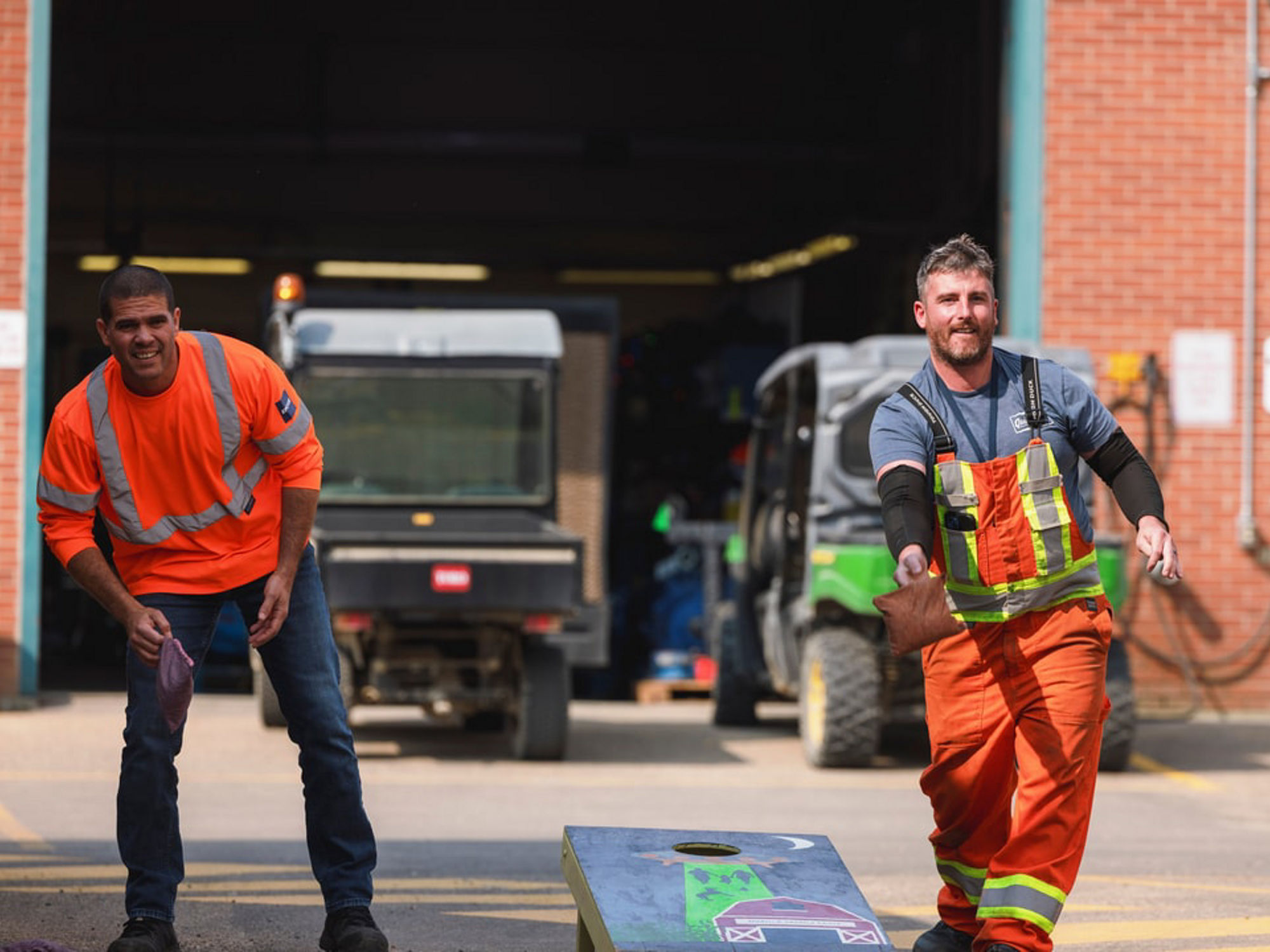 Two EPCOR employees wearing high-visibility safety apparel play cornhole during a United Way workplace fundraiser, promoting employee engagement and community giving.