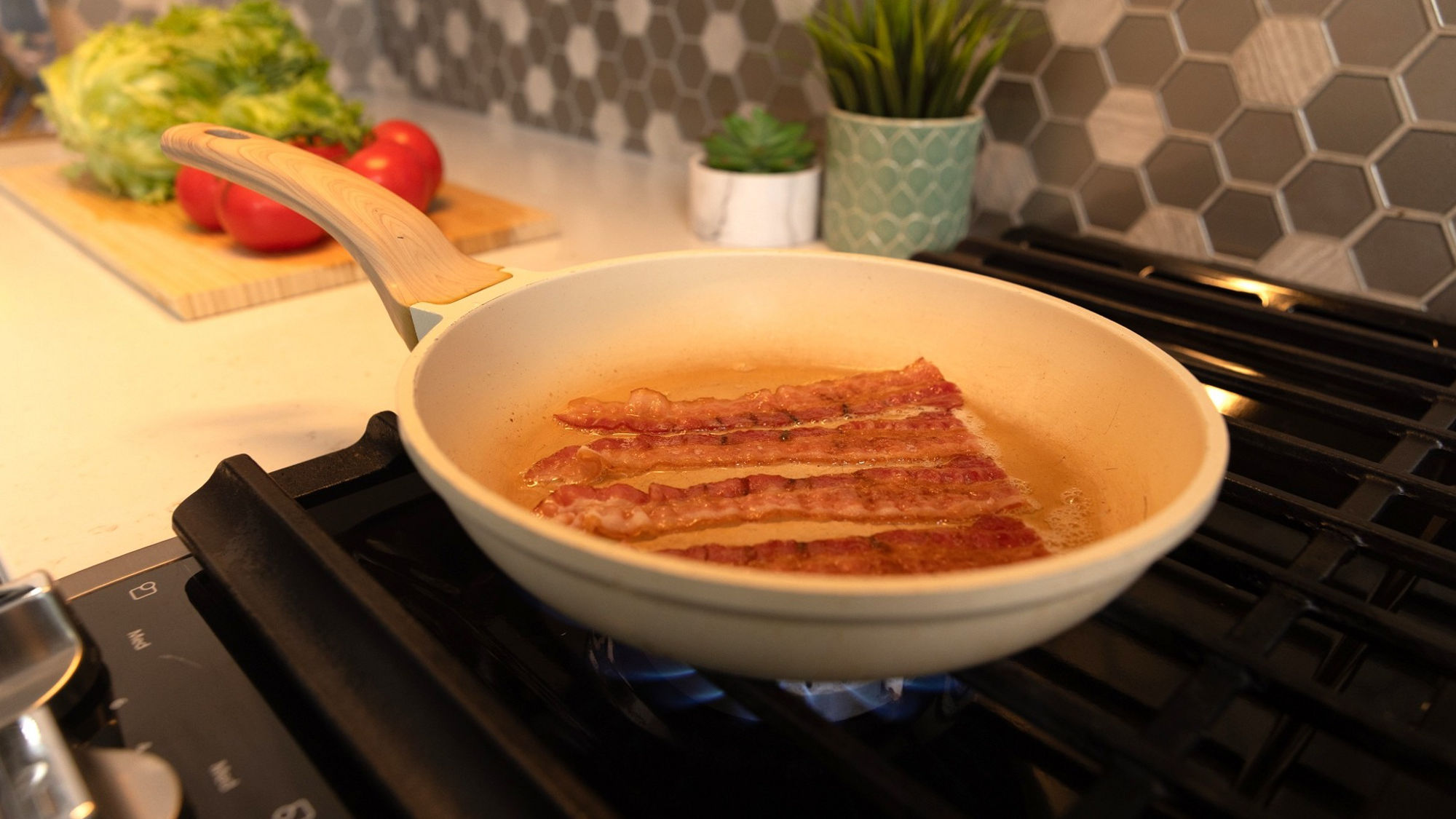 Bacon frying in a greasy pan on a stove.