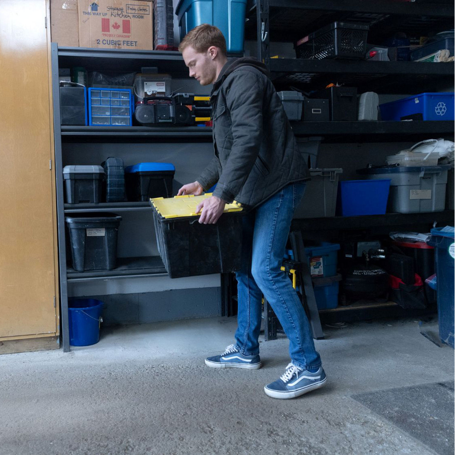A person organizes plastic storage bins on garage shelving in an effort to help protect belongings from water damage if flooding occurs.