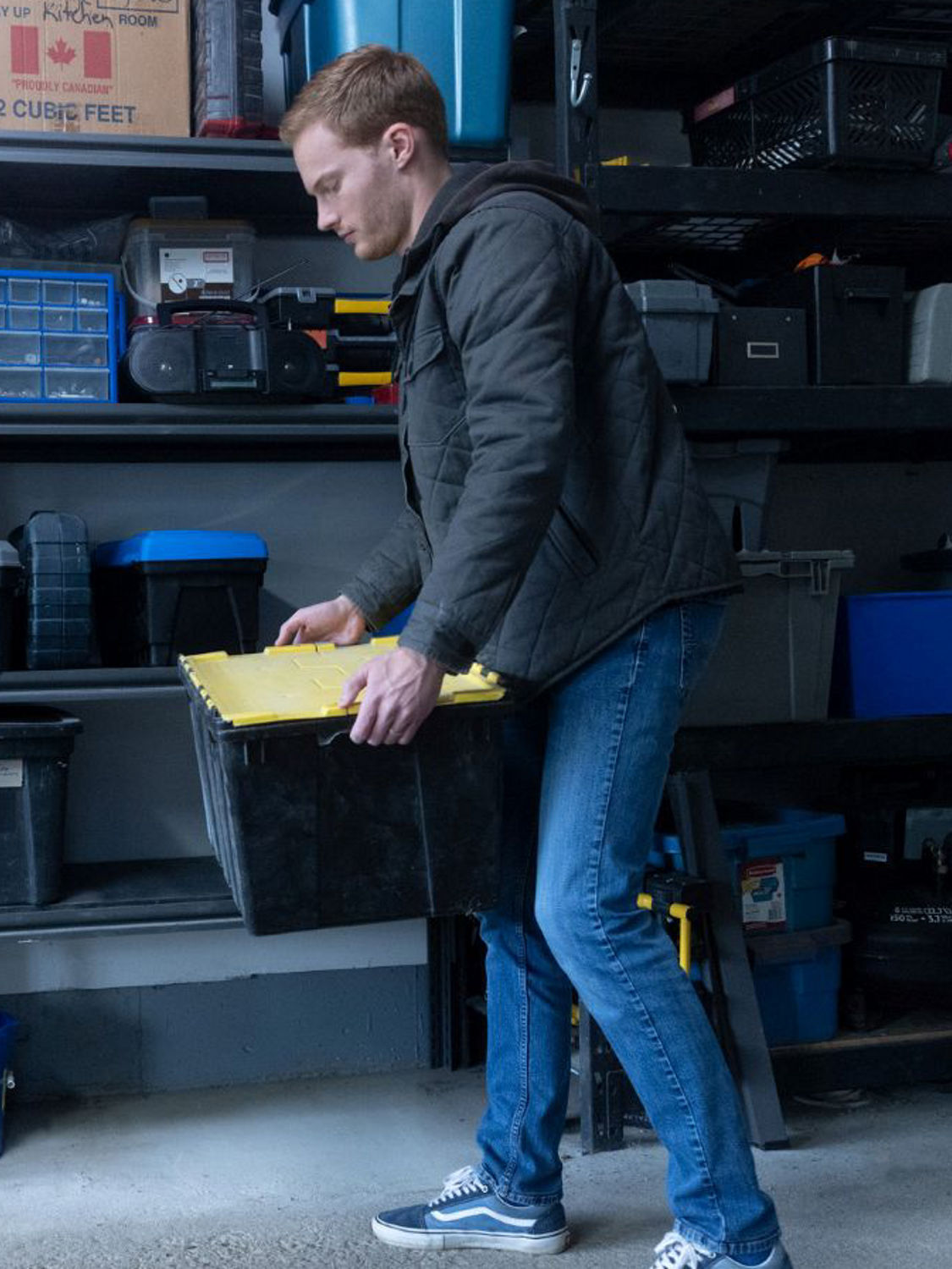 A person organizes plastic storage bins on garage shelving in an effort to help protect belongings from water damage if flooding occurs.