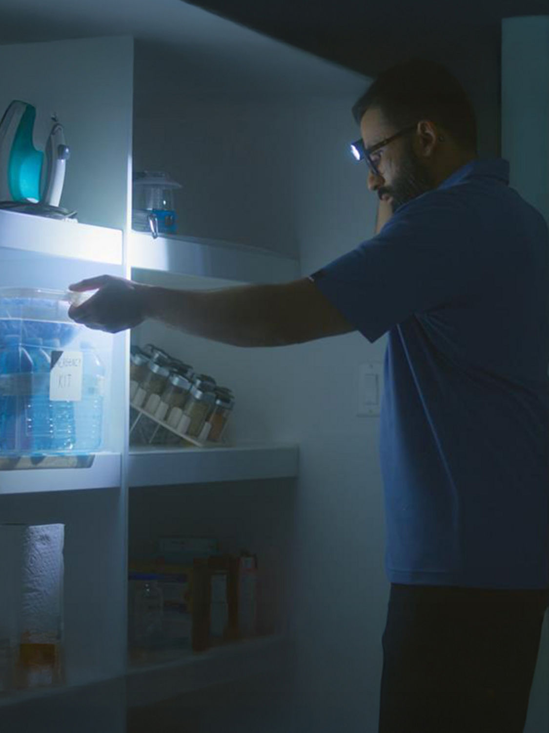A person with flashlight is getting their emergency kit off a shelf.