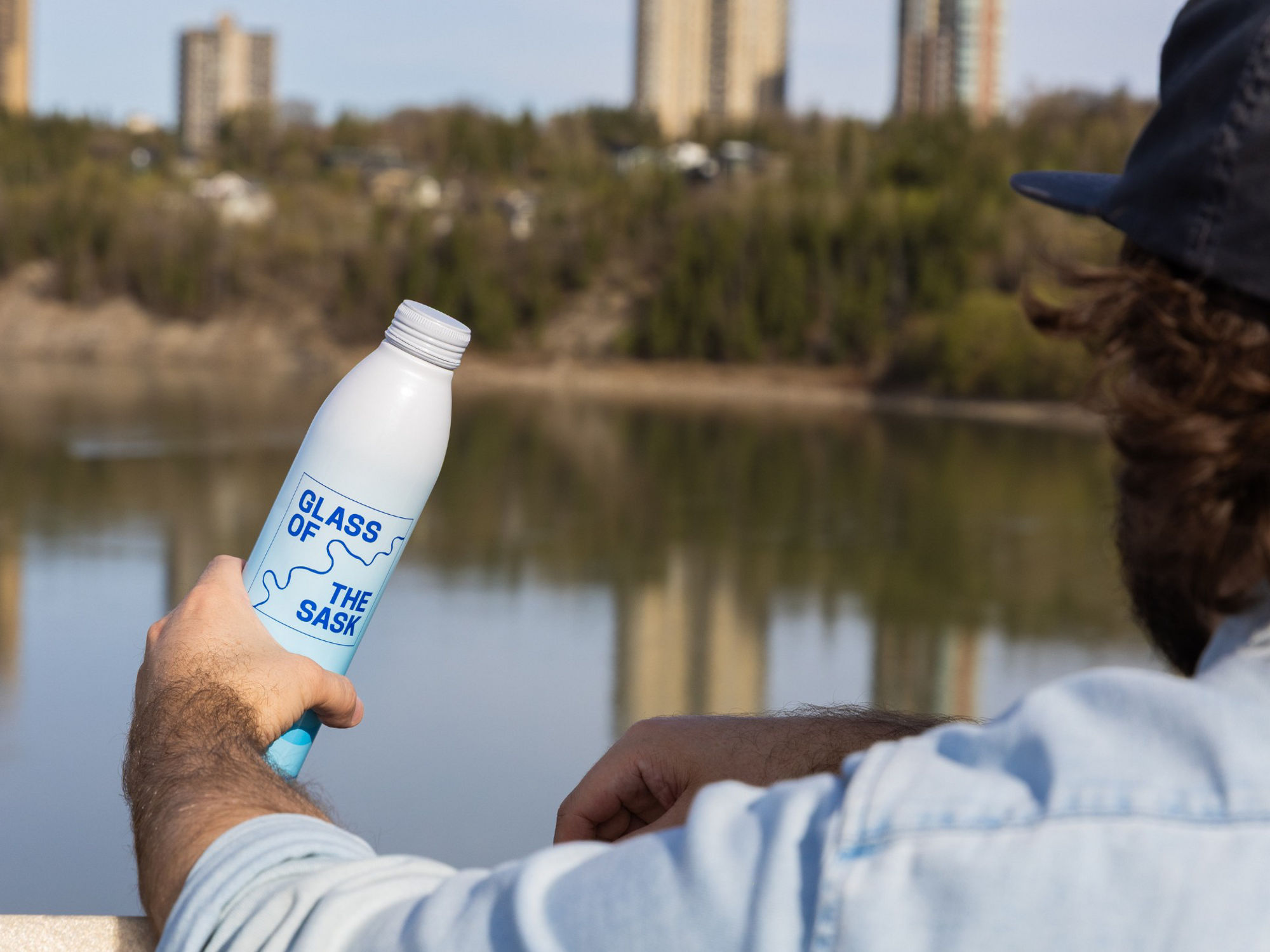 A Glass of the Sask water bottle being held up in front of the water tank at a festival.