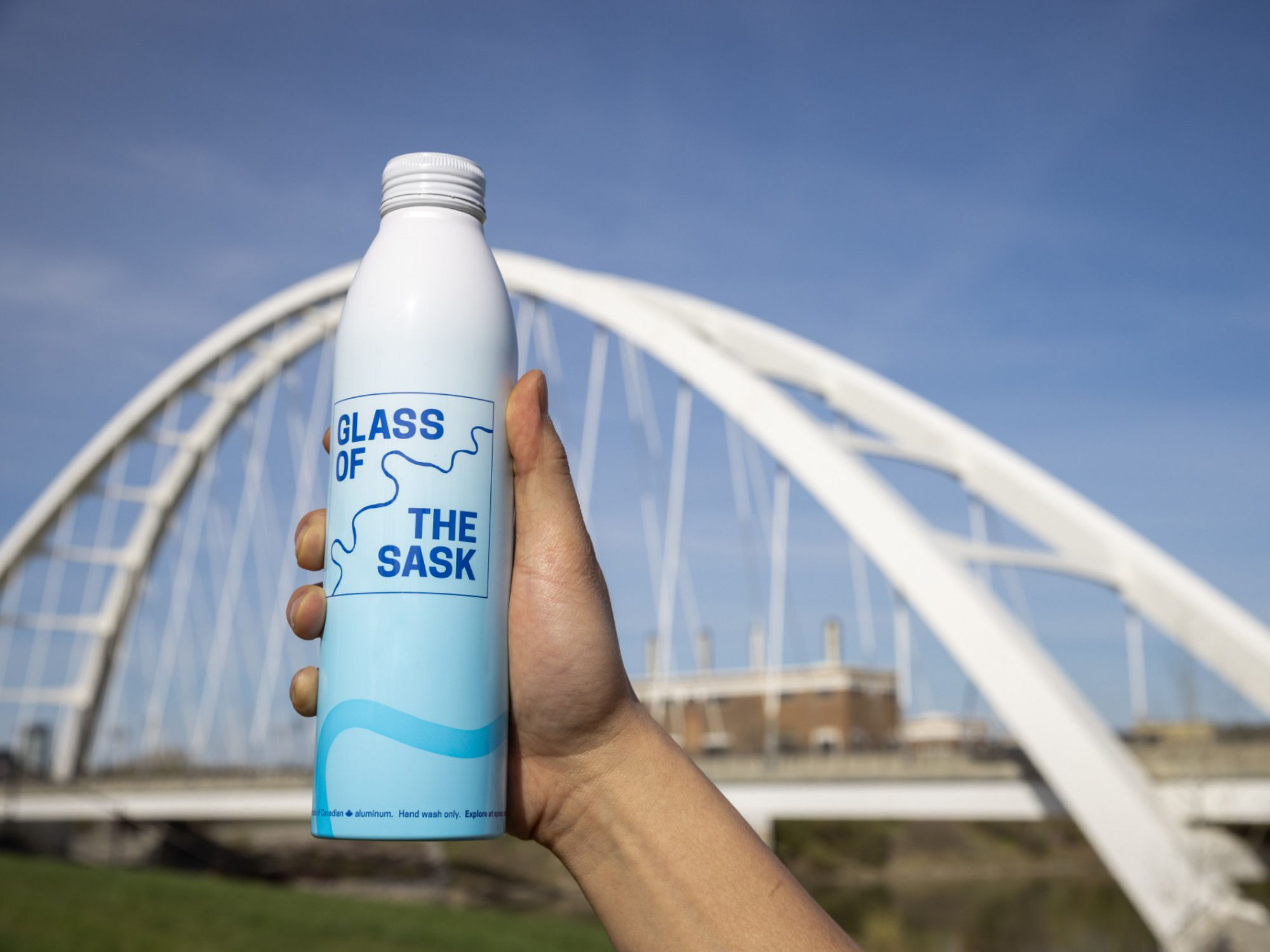 Person holding a Glass of the Sask aluminum in front of the Walterdale bridge in Edmonton.