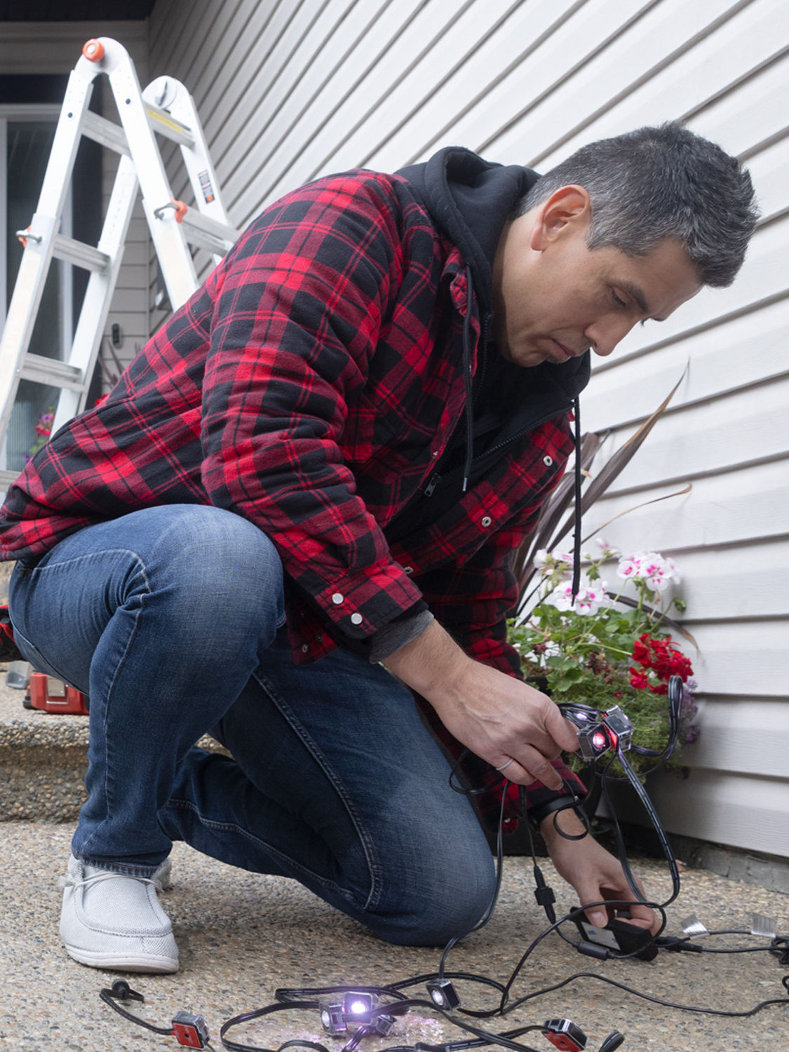A person crouched down to inspect holiday string lights before putting them up. 