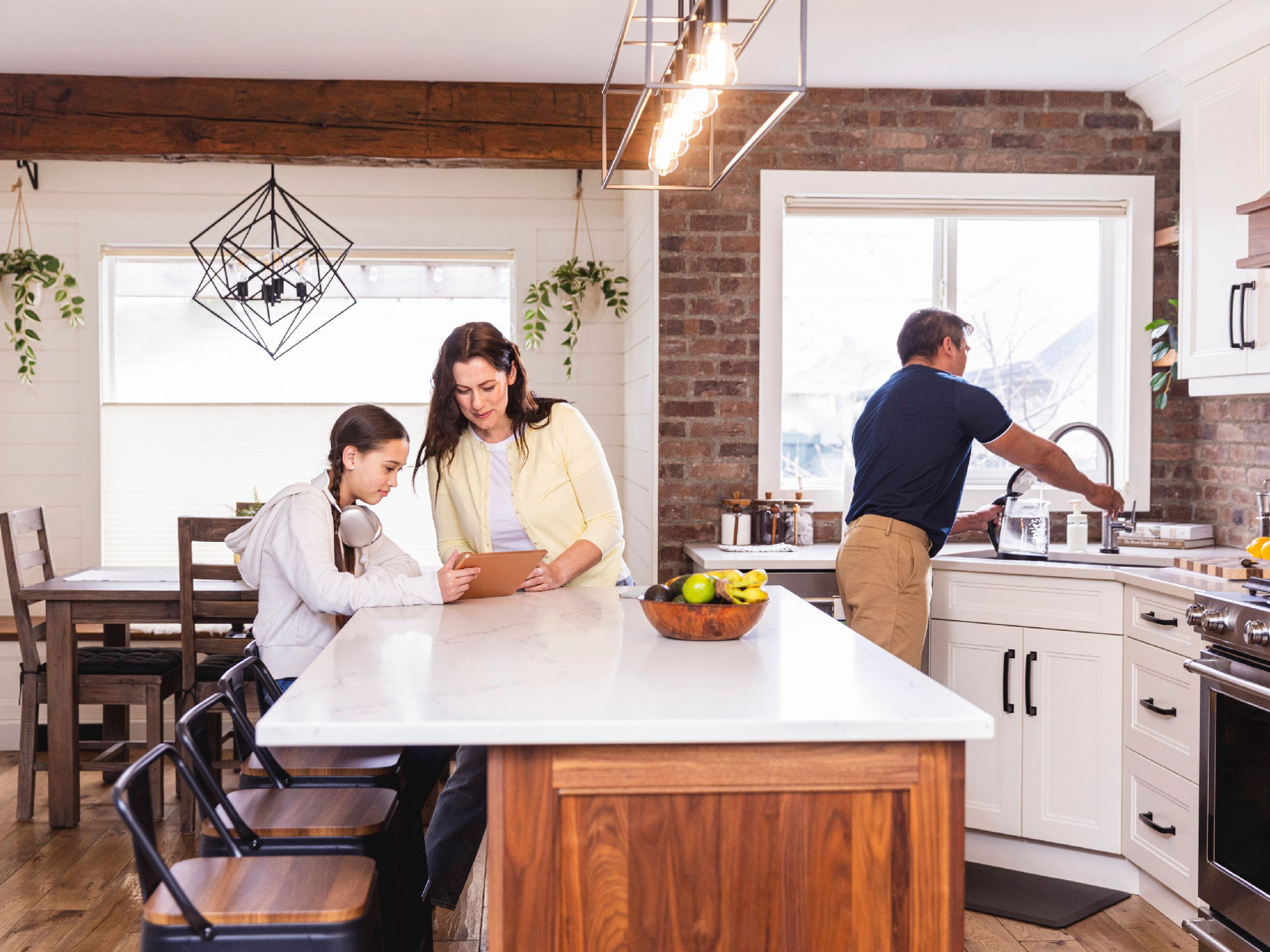 Mom and daughter on a tablet at kitchen island while Dad is cooking. 