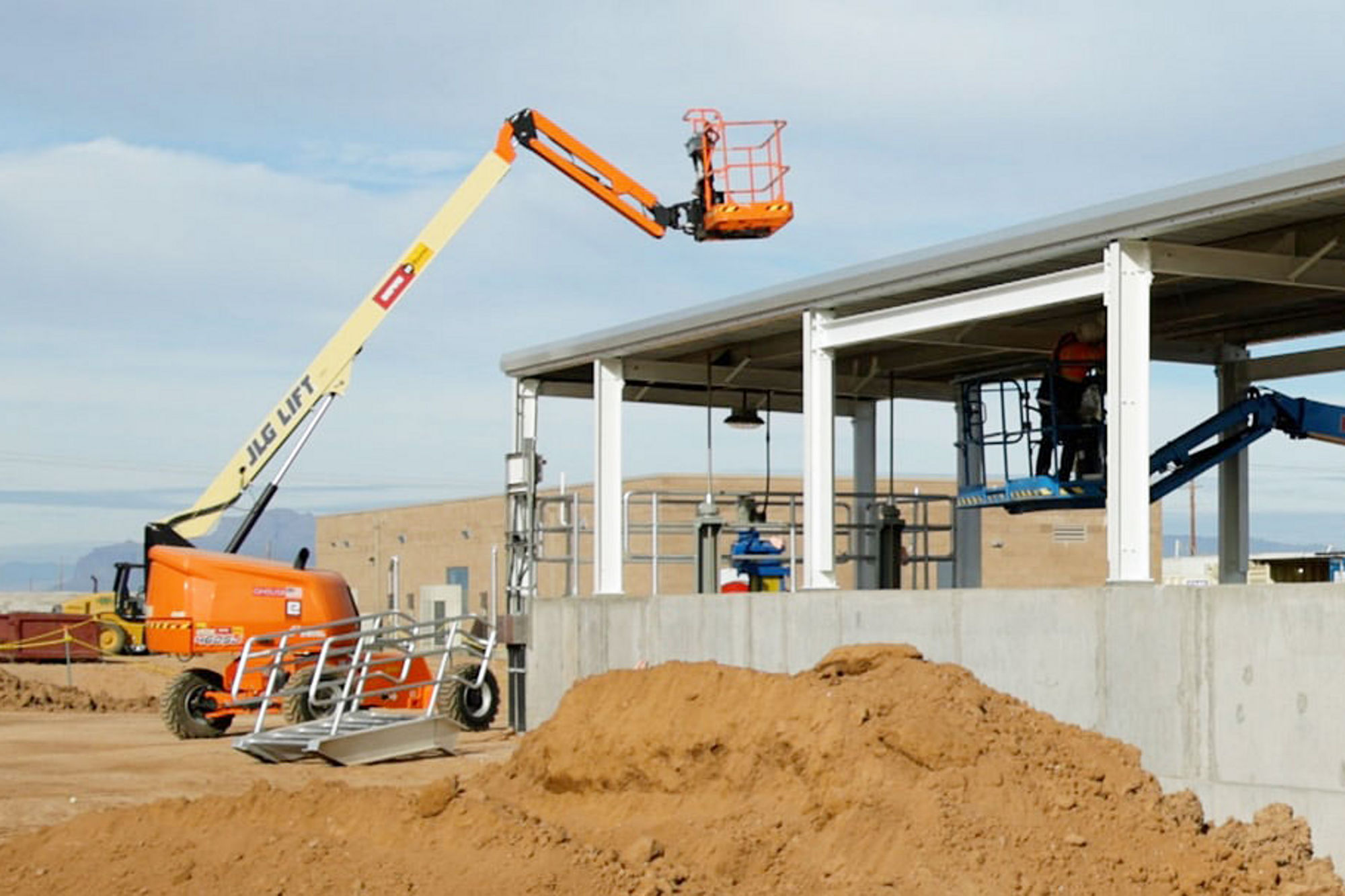 Construction equipment and aerial lifts are in use at a new property build, showing structural framing, concrete foundations, and active work on site.