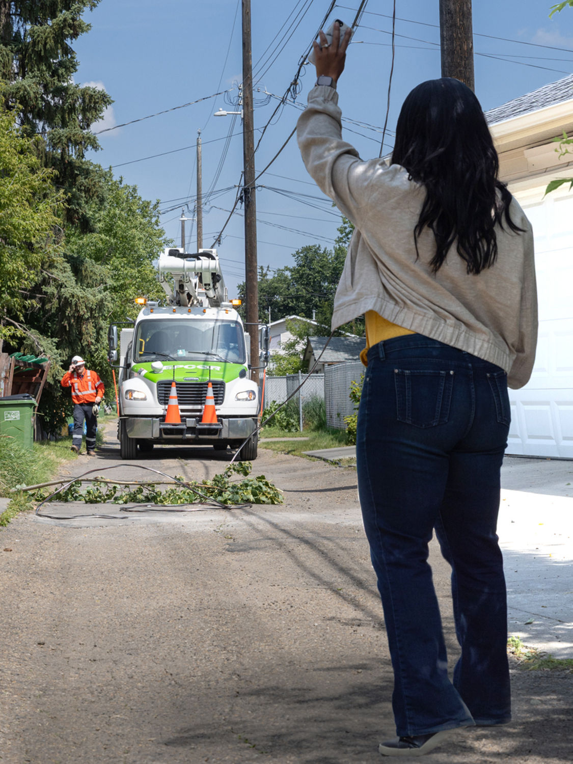 A person in an alley, flagging the power truck, keeping away from downed power lines.