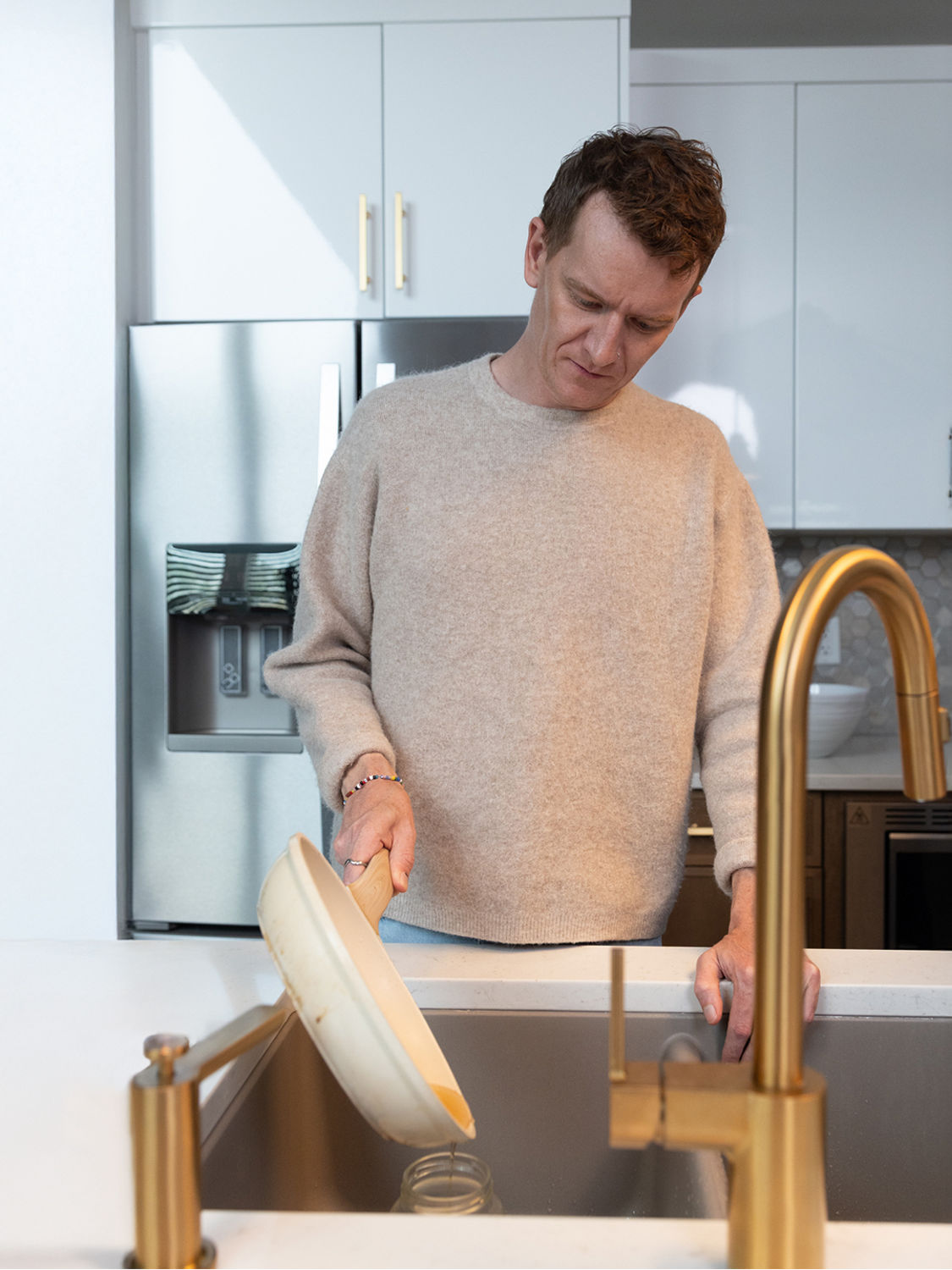 A person in a kitchen, pouring grease from pan into a glass jar.