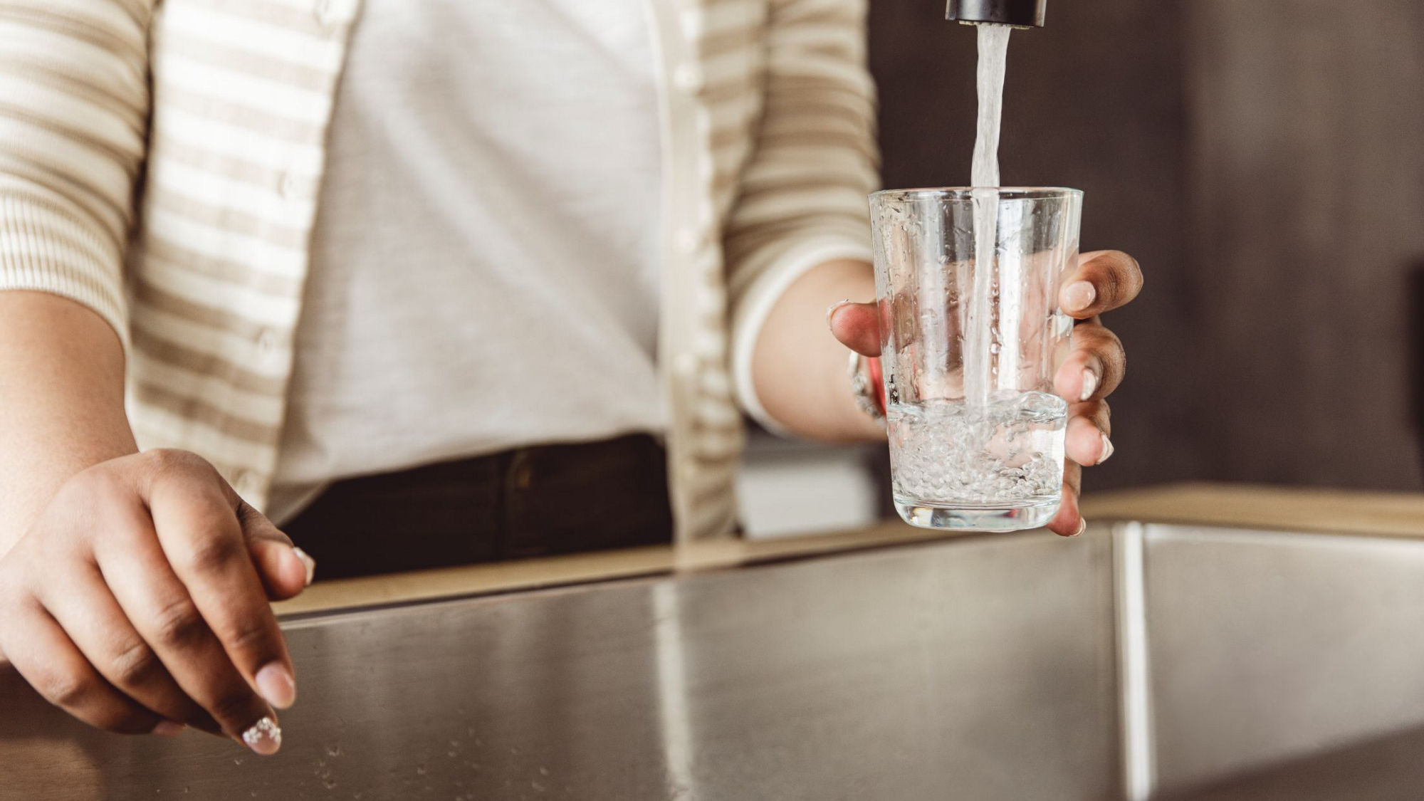 A person pouring water from a faucet into a glass, emphasizing hydration and clean tap water.