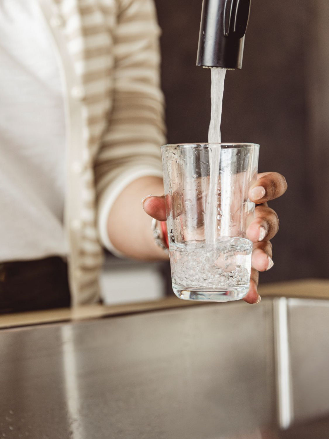 A person pouring water from a faucet into a glass, emphasizing hydration and clean tap water.