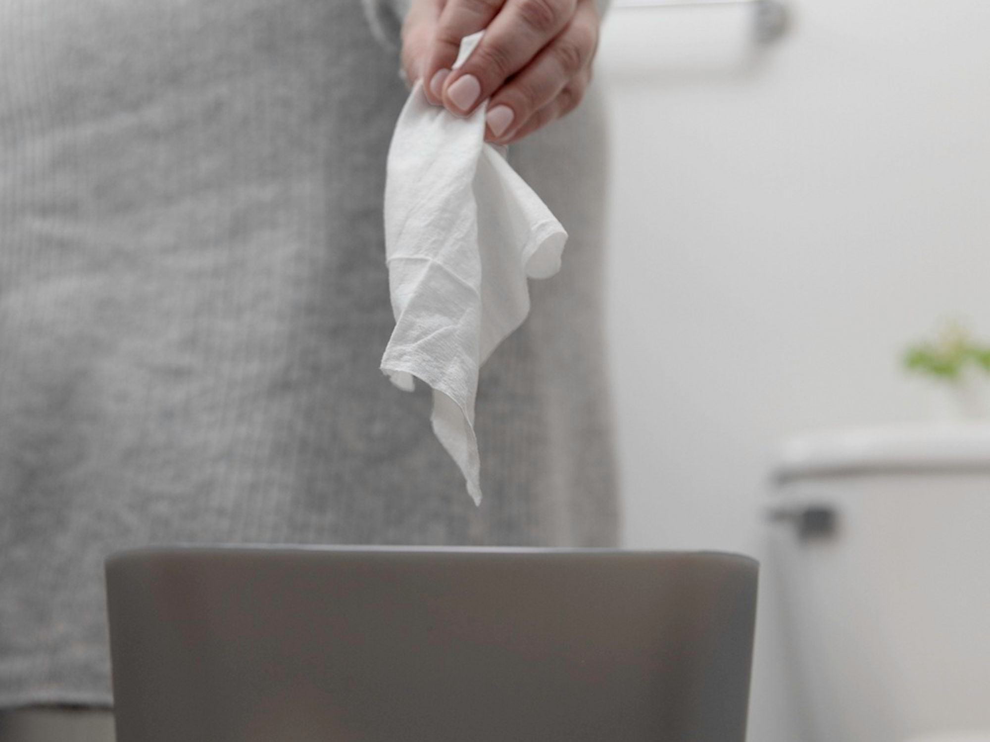 Someone correctly throwing a wipe into a garbage can. Toilet is in background.