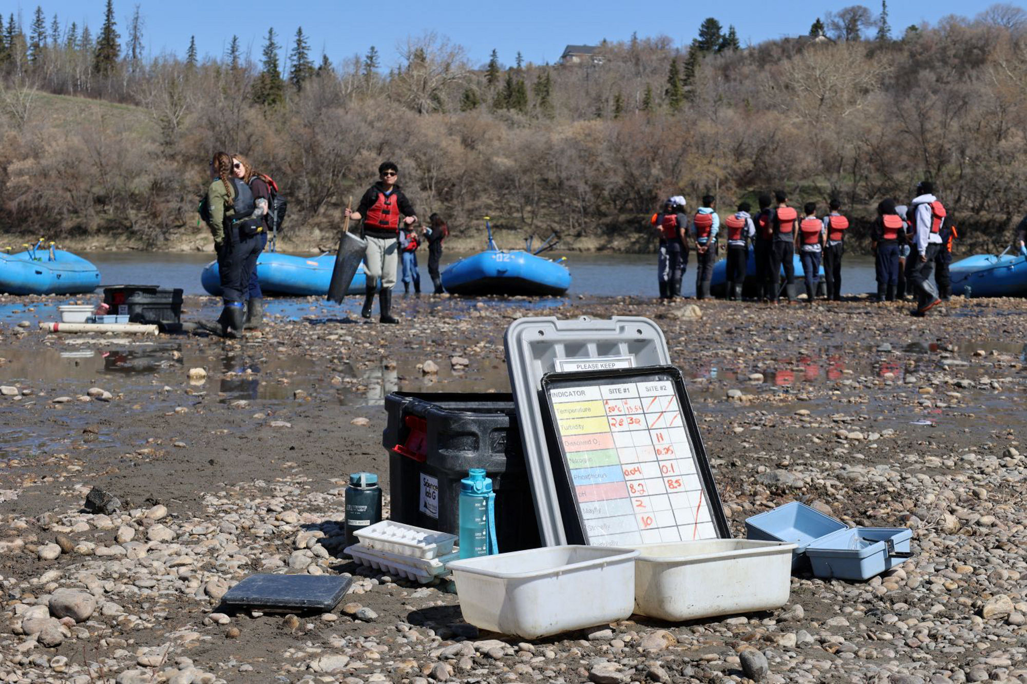Testing kit set up on the bank of the North Saskatchewan River with students near rafts in the background.