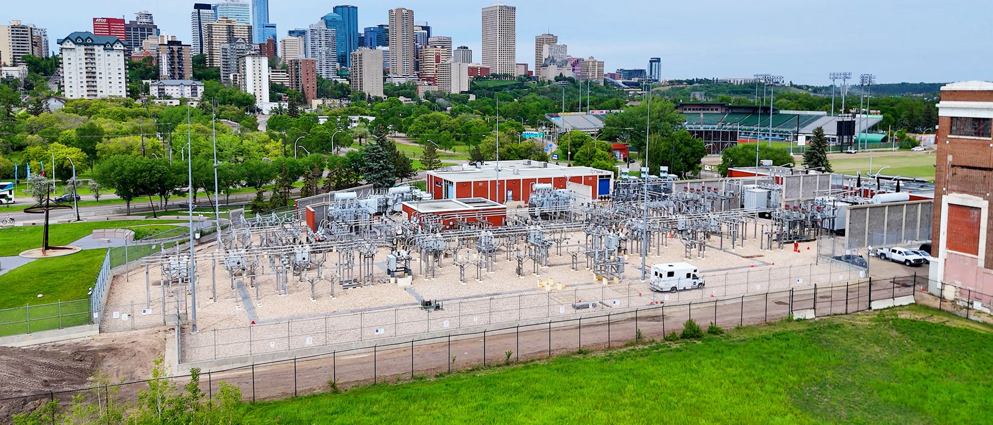 Aerial view of the Rossdale electrical substation in Edmonton with the downtown skyline, green parkland, and nearby sports facilities in the background.