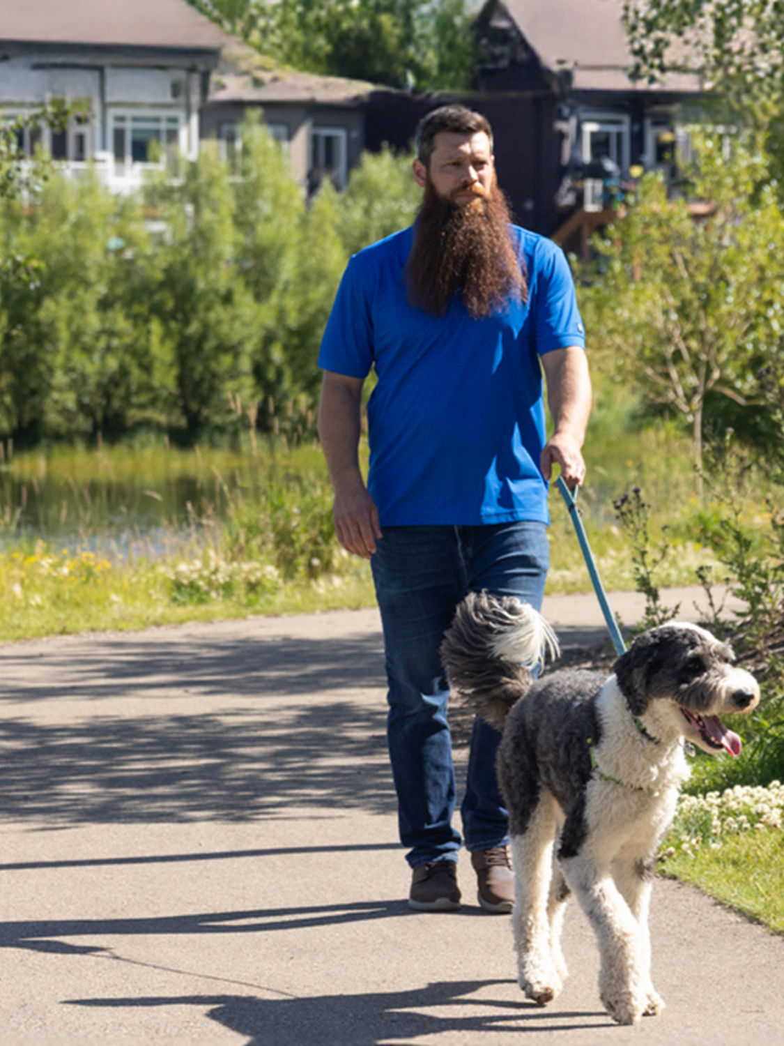 A person walking a dog on a path near a stormwater pond.