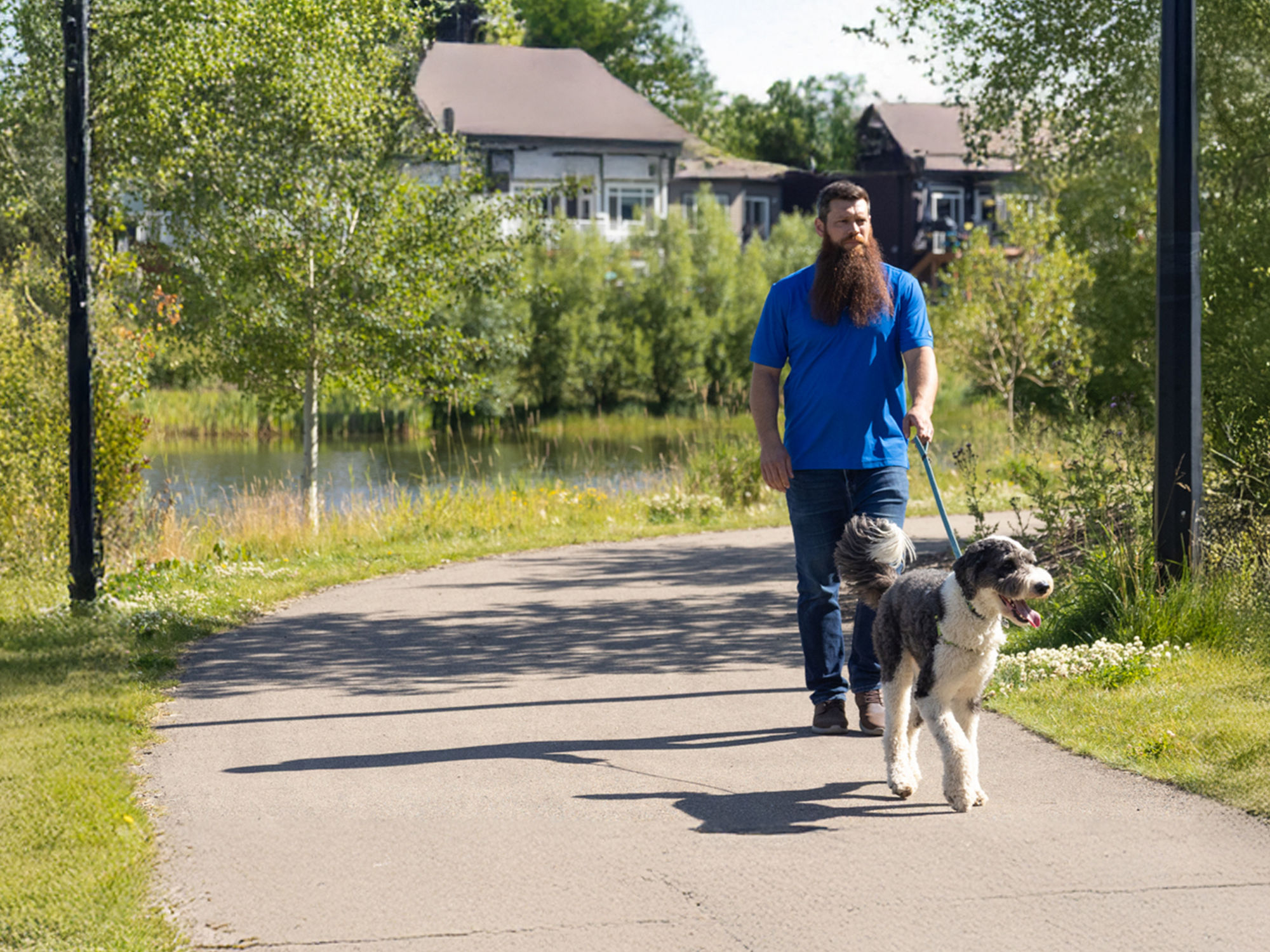 A person walking a dog on a path near a stormwater pond.
