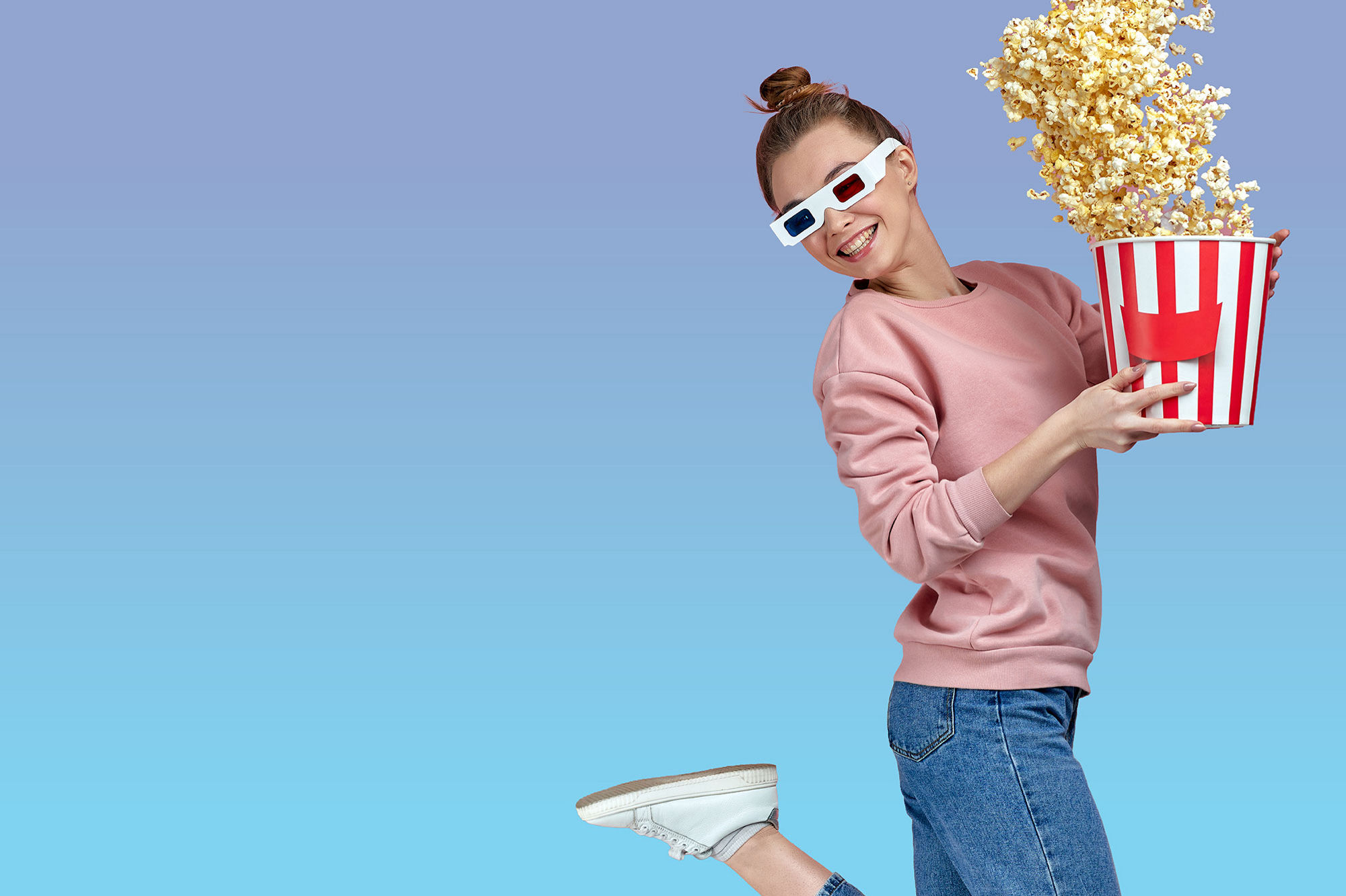 Person wearing 3D glasses holds a large bucket of popcorn against a bright blue background, evoking a fun movie night or cinema experience.