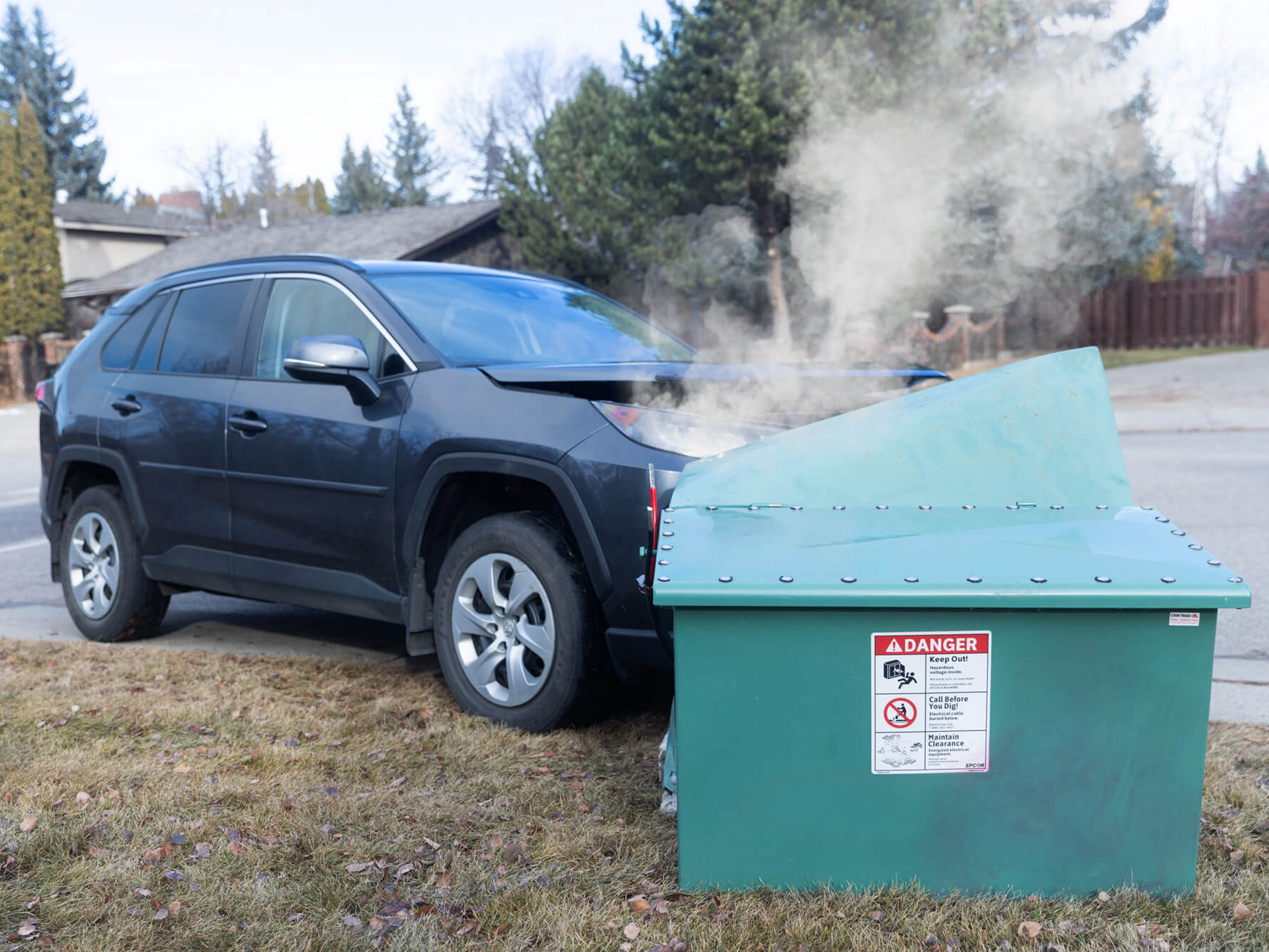 A car has run into a green electrical box in a neighbourhood. Both have damage.